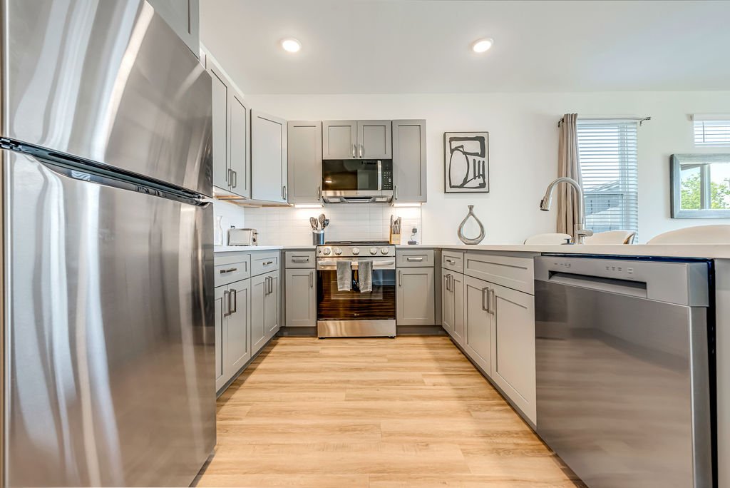 Modern kitchen with stainless steel refrigerator, microwave, oven, and dishwasher, gray cabinets, white countertops, and hardwood floors.