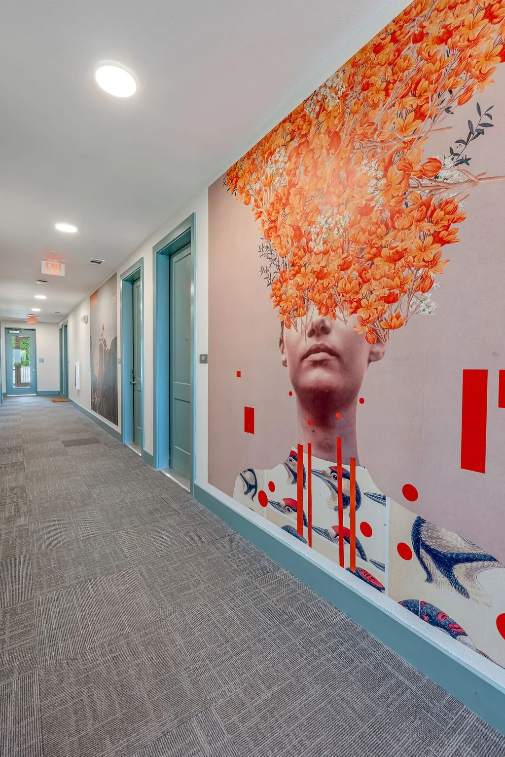 Hallway with blue doors and large wall art of a person's face with orange flowers as hair, abstract red shapes, and fish designs.