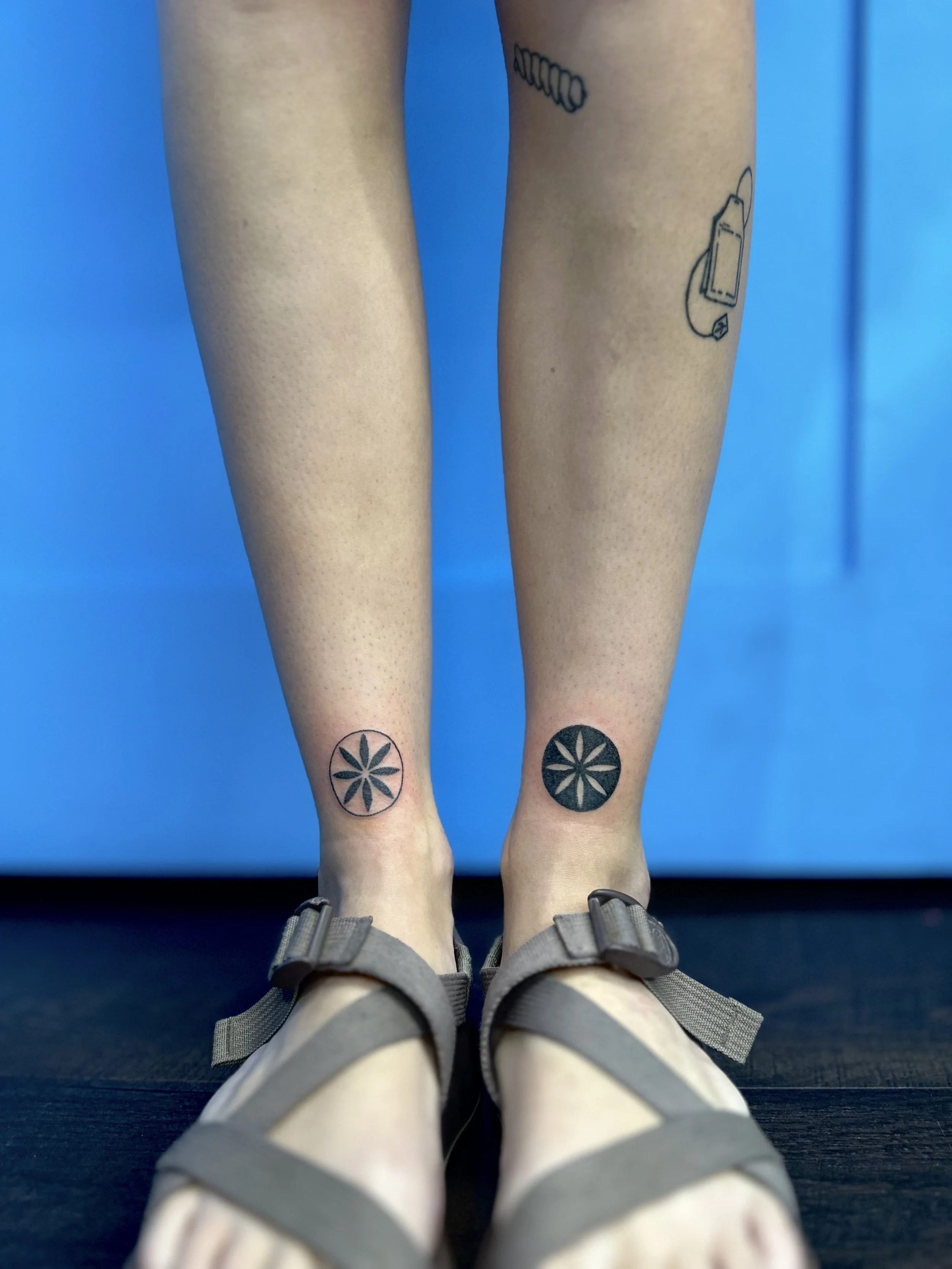 tattoo of a two symmetrical flower designs on a persons ankles