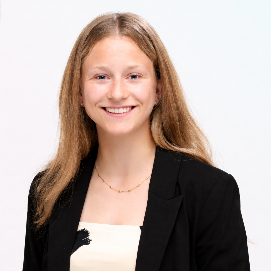 Junge Frau mit langen, glatten, roten Haaren, dunklem Blazer und weißem Top, lächelnd vor weißem Hintergrund.