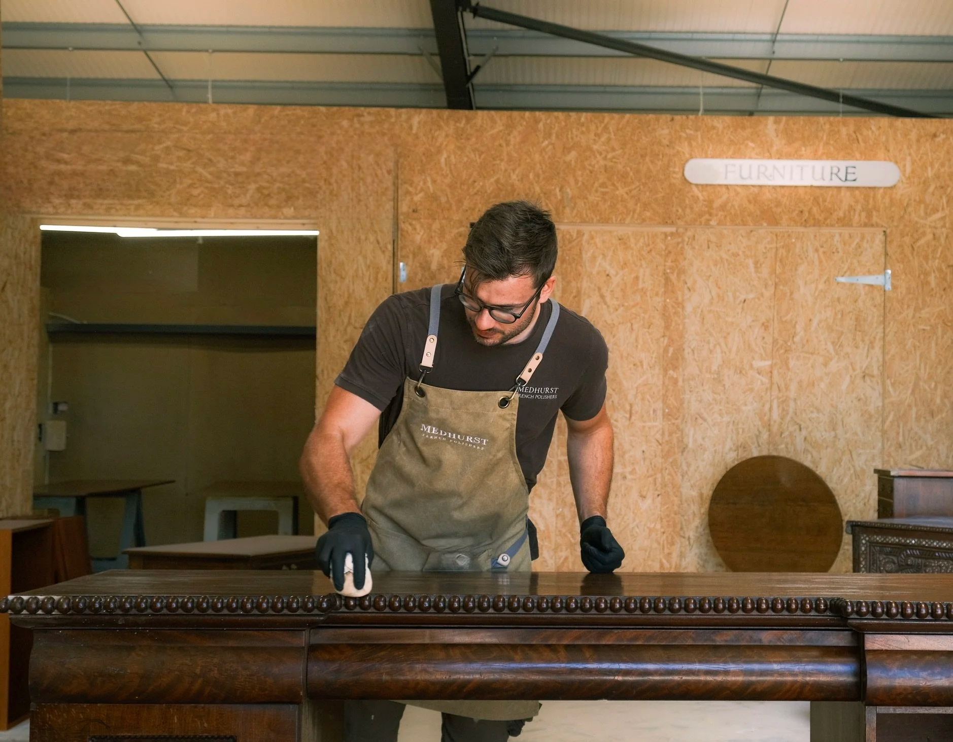 Person applying finish to wooden table with cloth wearing blue gloves