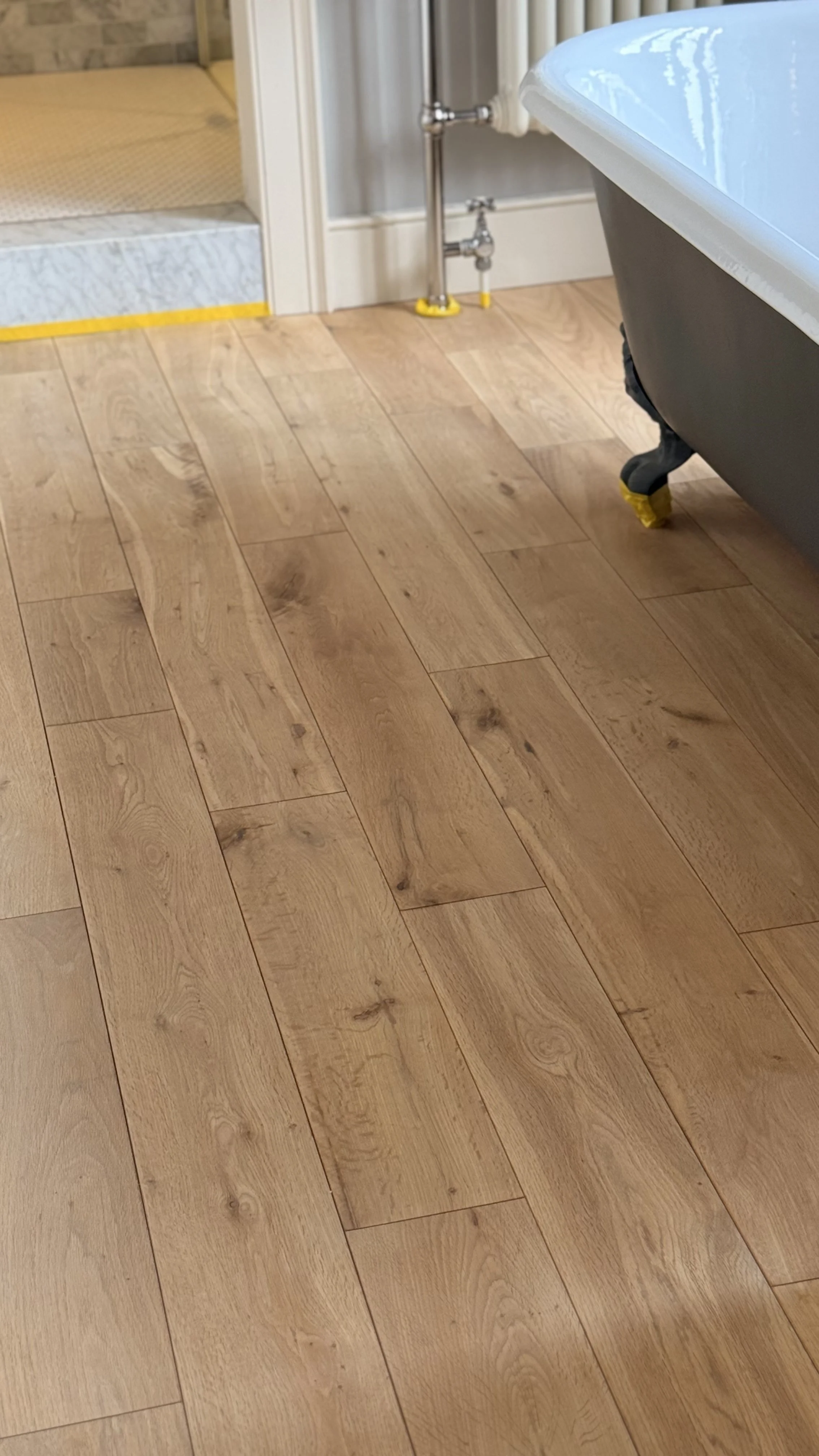 A wooden floor with a loose plank resting on top, showing grain patterns and natural wood color.