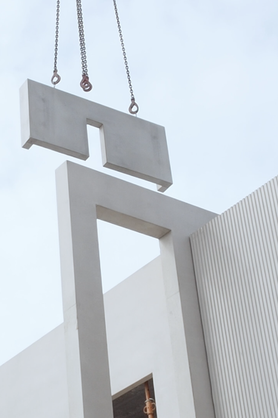 Estructuras de concreto en construcción, con cadenas y ganchos de izaje, junto a una pared de metal corrugado.