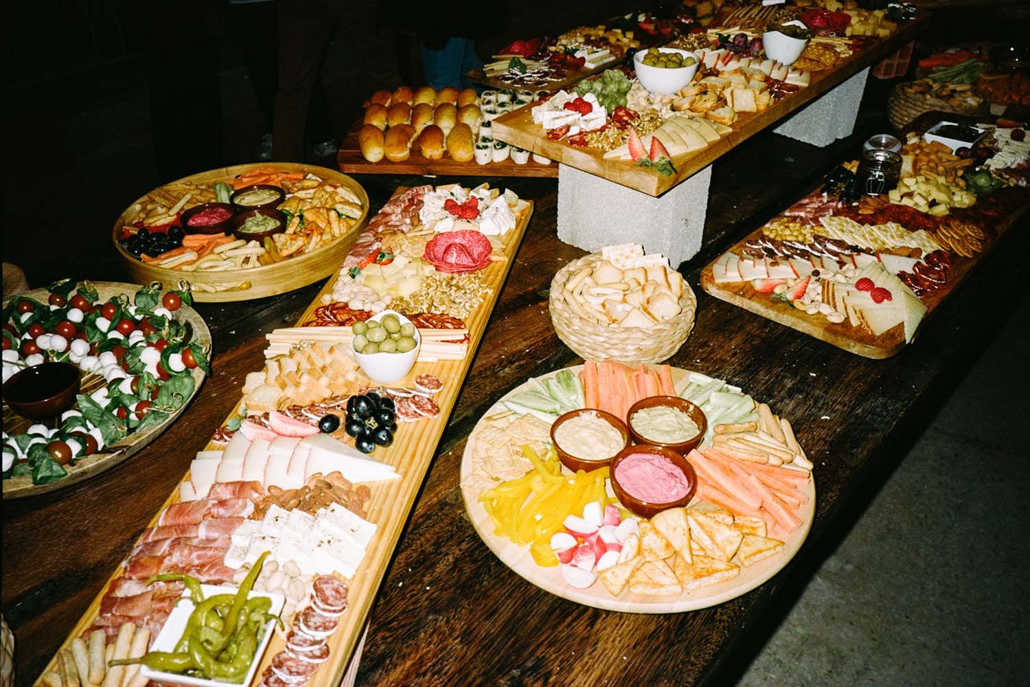 Mesa con varios platos de charcutería, quesos, embutidos, vegetales, panes y salsas.