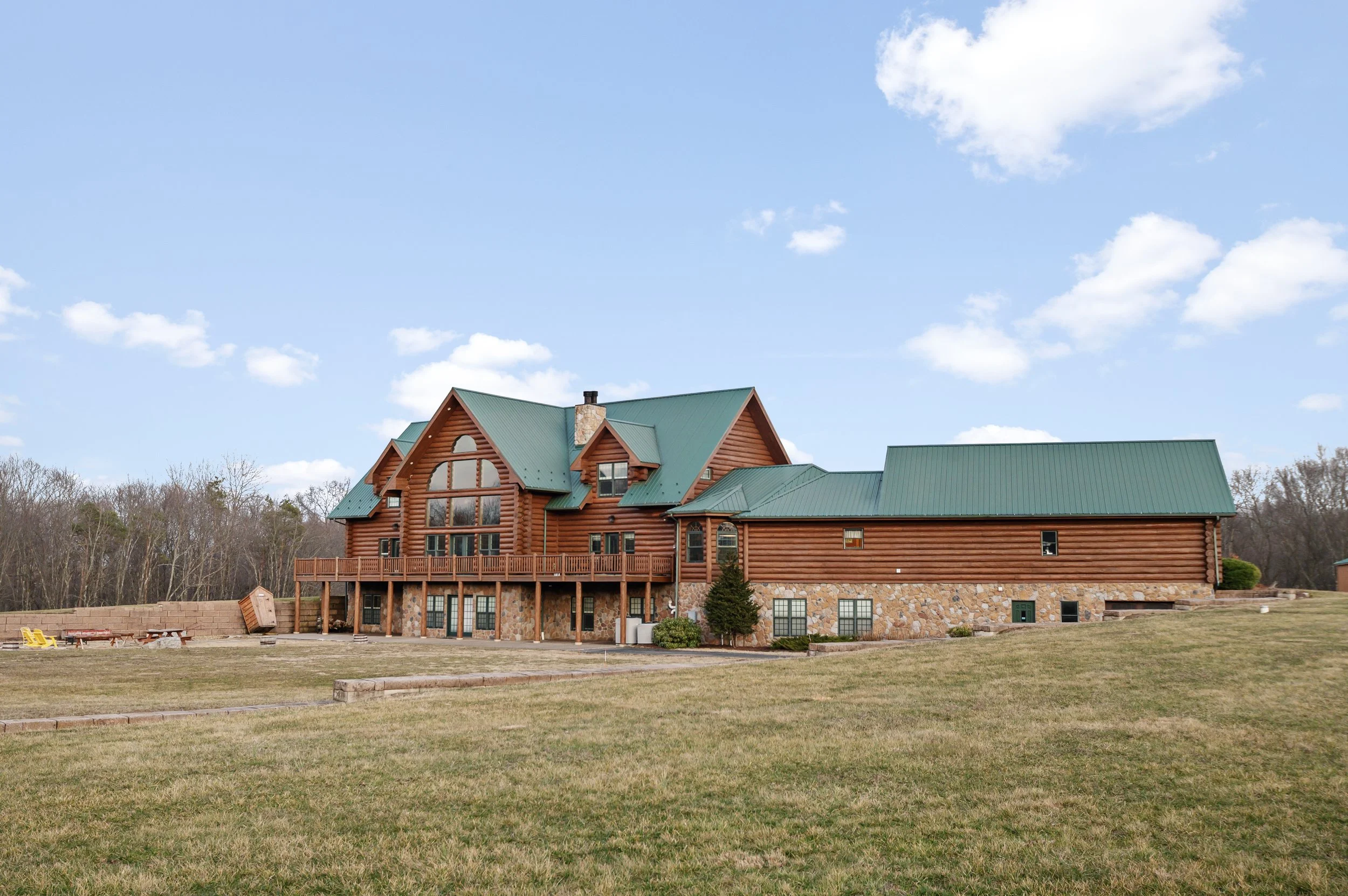 A large wooden house with a green metal roof sitting on a grassy lawn, with a blue sky and some clouds overhead.