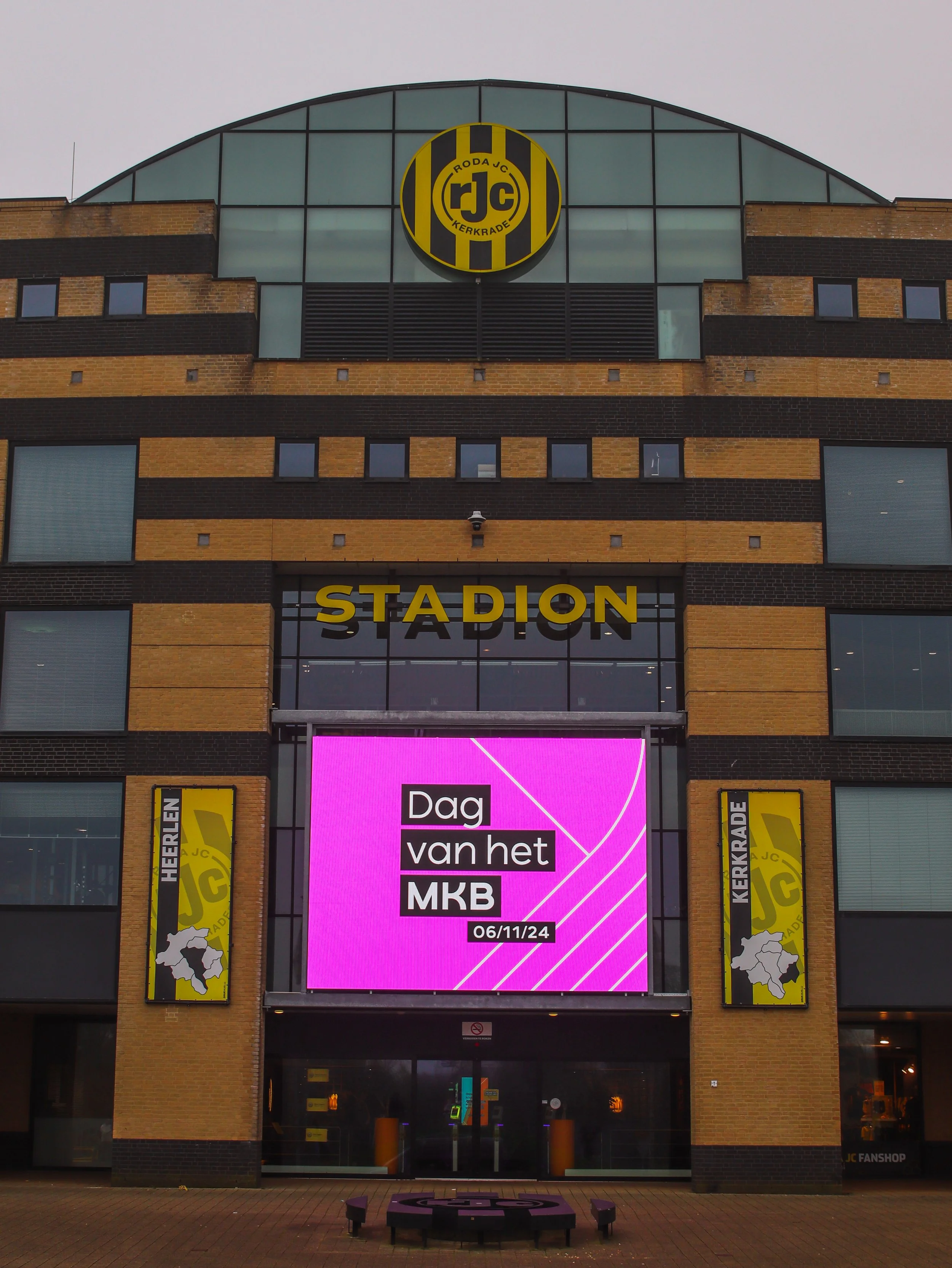 De gevel van een stadion met een LED-scherm dat een mededeling toont en het logo van Roda JC Kerkrade erboven.