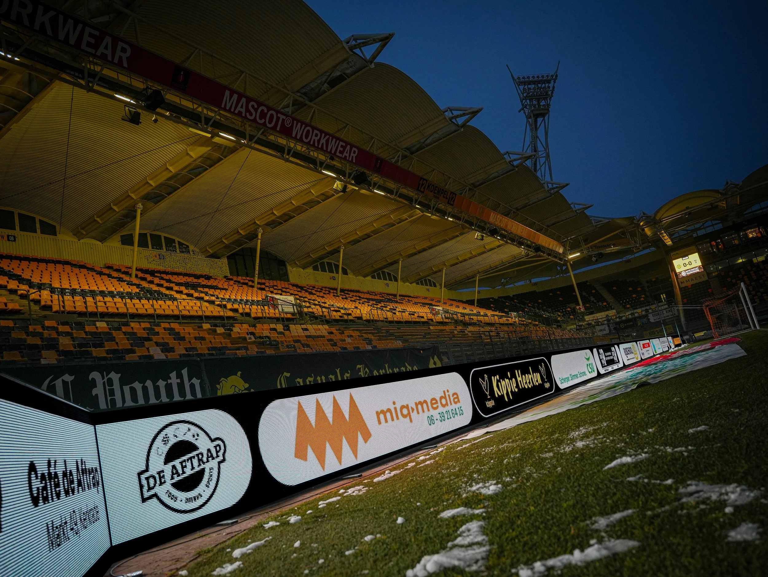 Leeg voetbalstadion tijdens avond met verlichte reclameborden en lege stoelen.