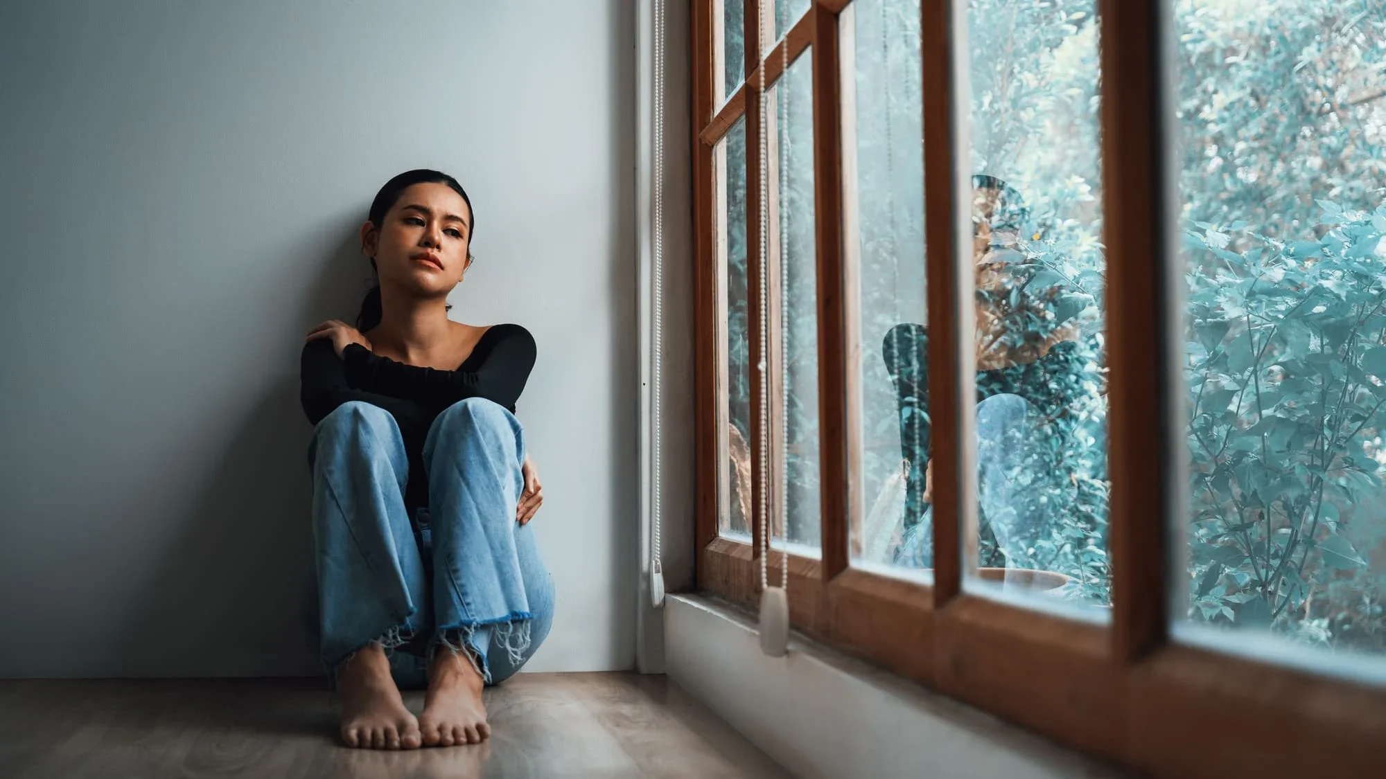 A person sitting on the floor beside a window, looking withdrawn and exhausted, reflecting the emotional weight of seasonal depression and the need for winter mental health support in Philadelphia and Bryn Mawr.