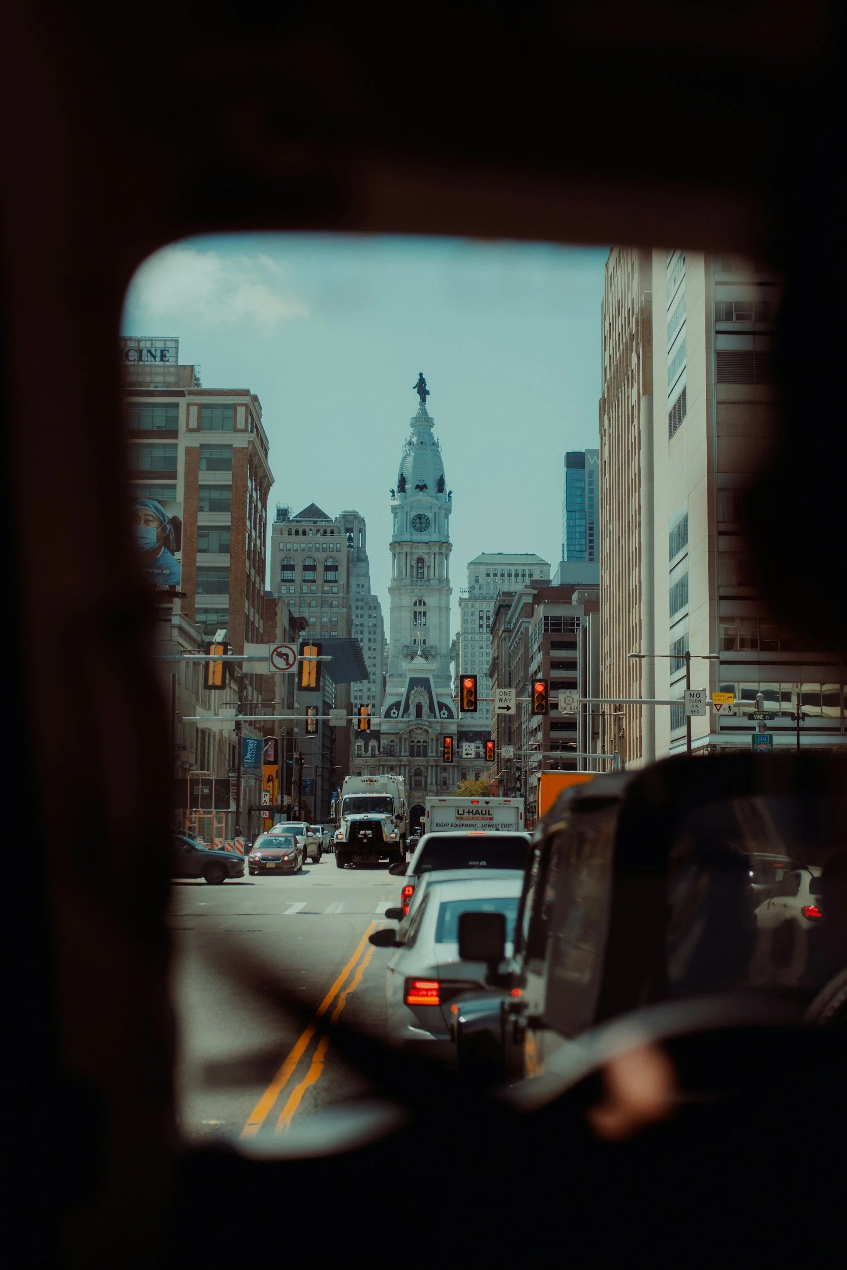 View of Philadelphia City Hall down a busy Center City street, seen through a car windshield with traffic in the foreground.