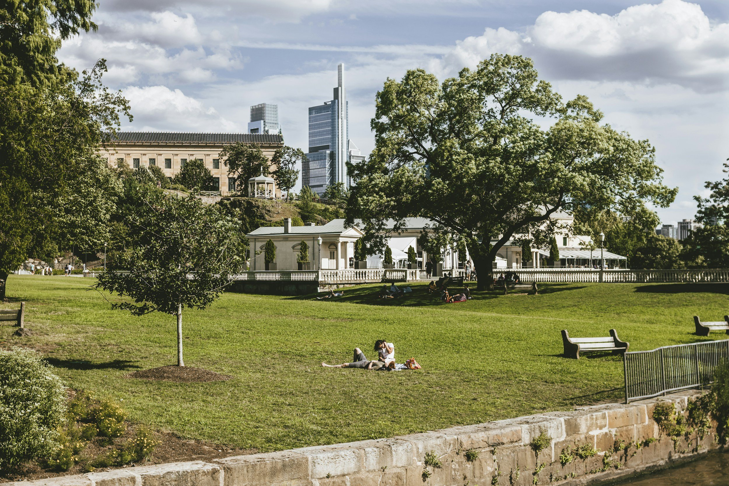 People relaxing in a sunlit Philadelphia park during summer, representing spaciousness for deeper trauma therapy work.