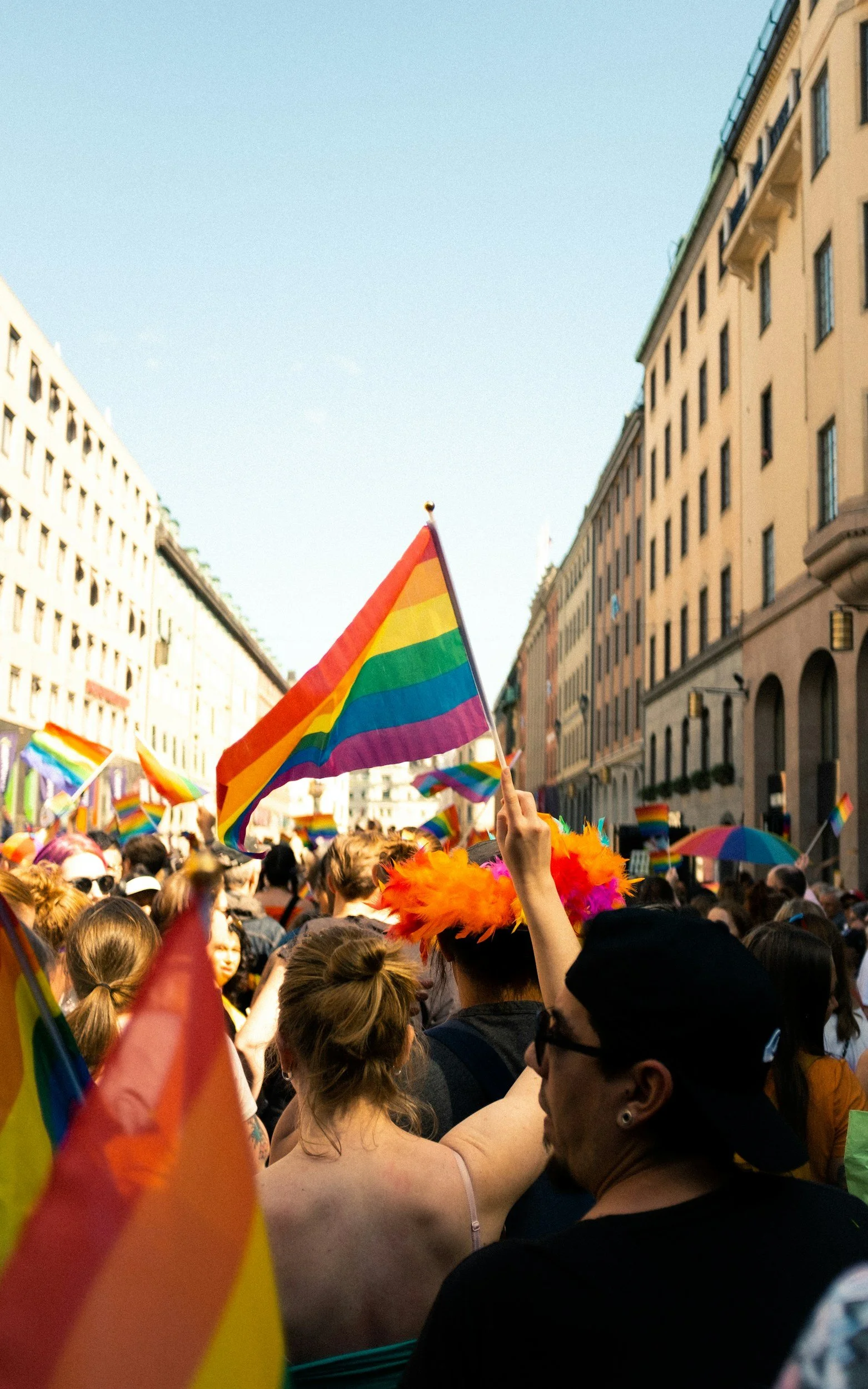 People celebrating Pride while holding rainbow flags, representing LGBTQIA+ community, belonging, and affirming mental health support.