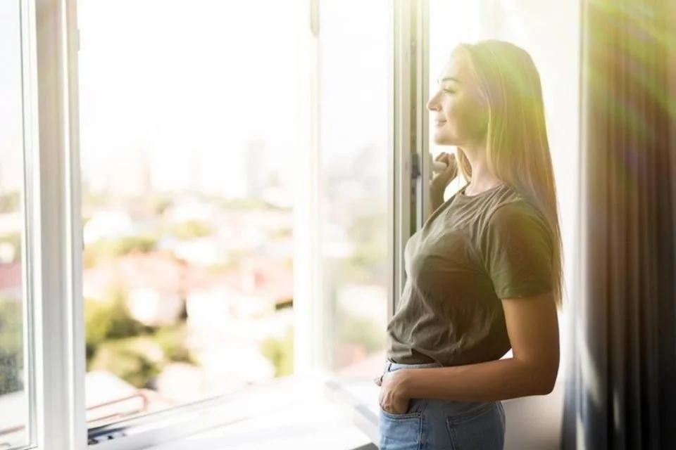 A person standing near a bright window with sunlight streaming in, symbolizing light therapy, renewed energy, and healing from seasonal affective disorder for people in Philadelphia, Bryn Mawr, and the Main Line.