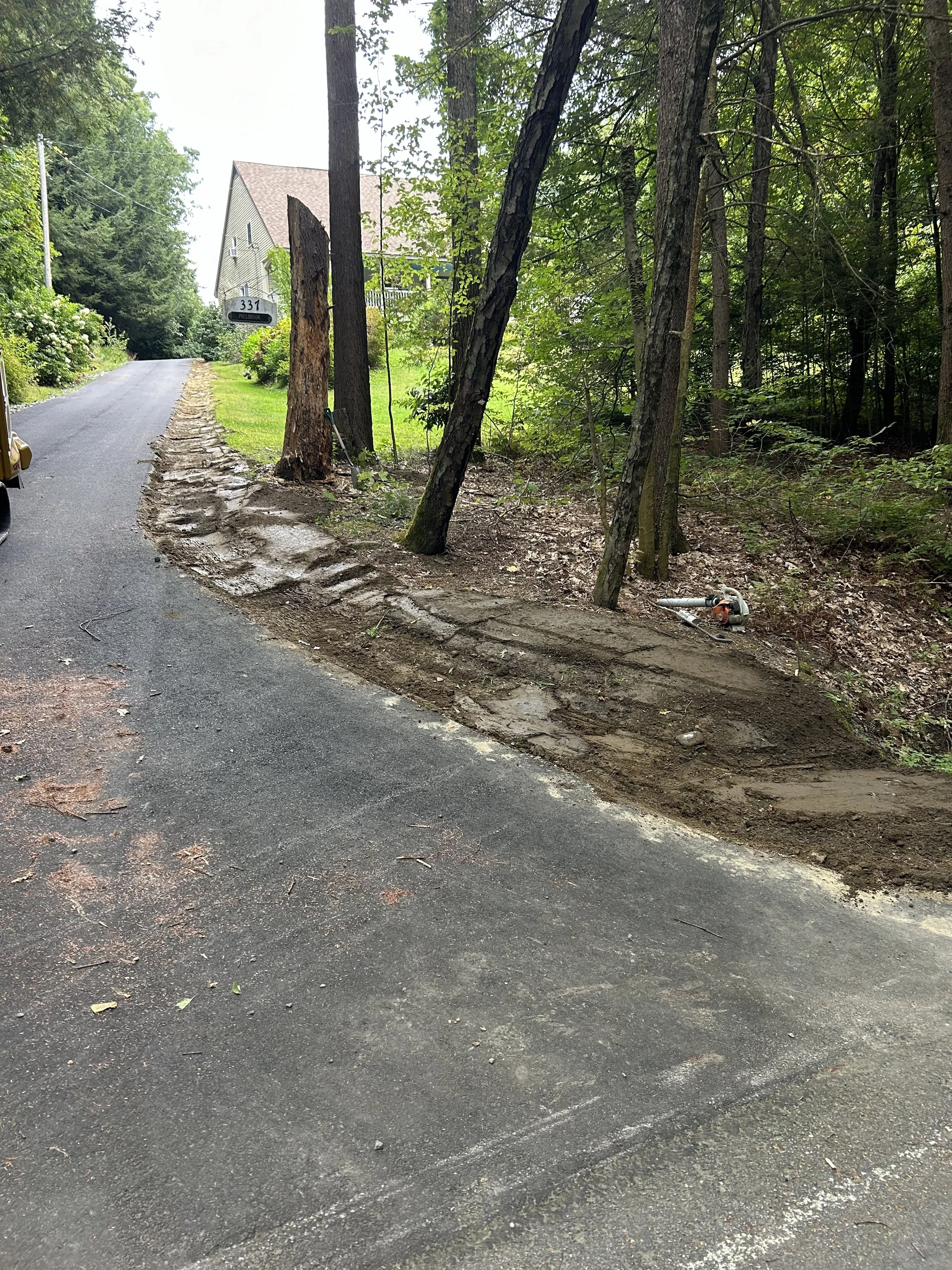 A road undergoing repair with new pavement and a section of dirt and gravel on the side, surrounded by trees and greenery.