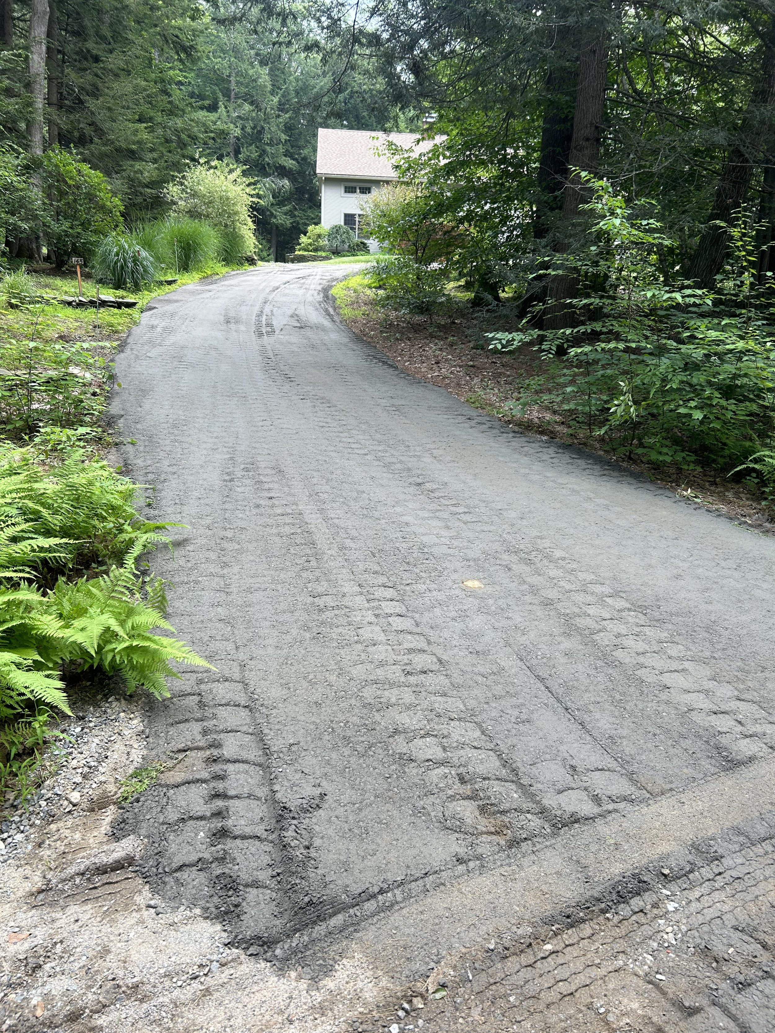 A gravel driveway curves uphill towards a house surrounded by trees and greenery.