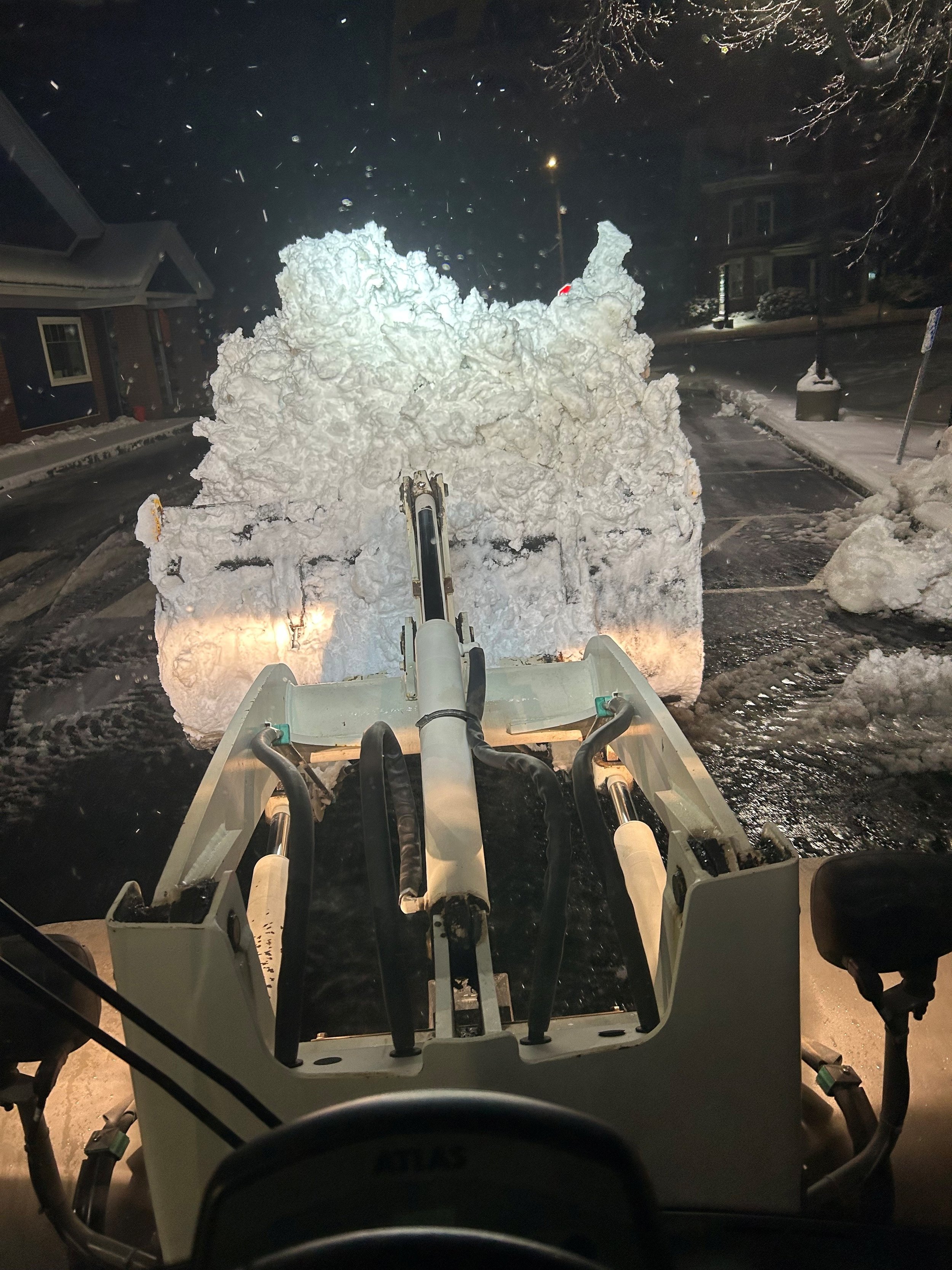 A snowplow clearing snow from a residential street at night.