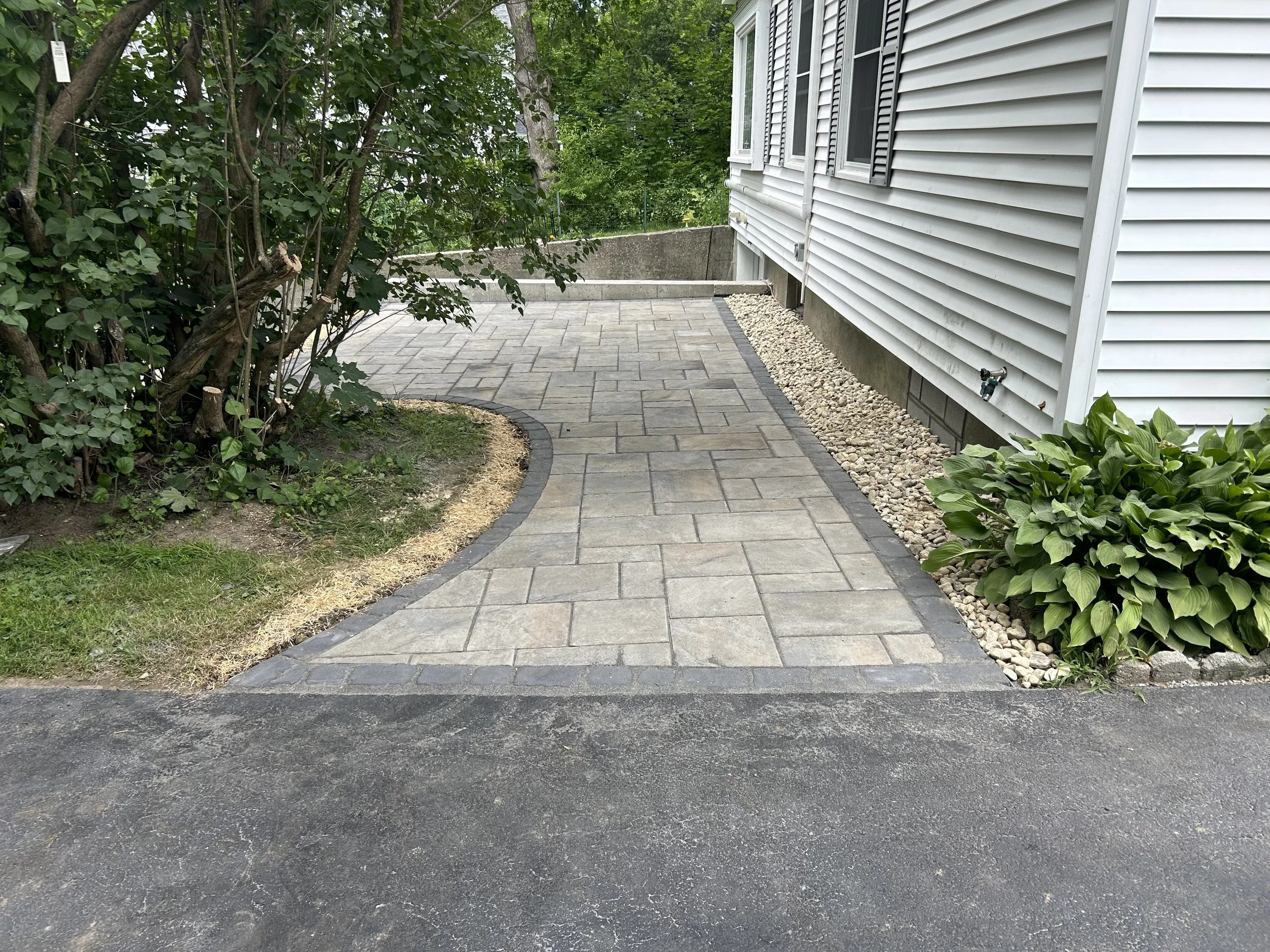 Newly paved concrete walkway with landscaped garden and house siding.