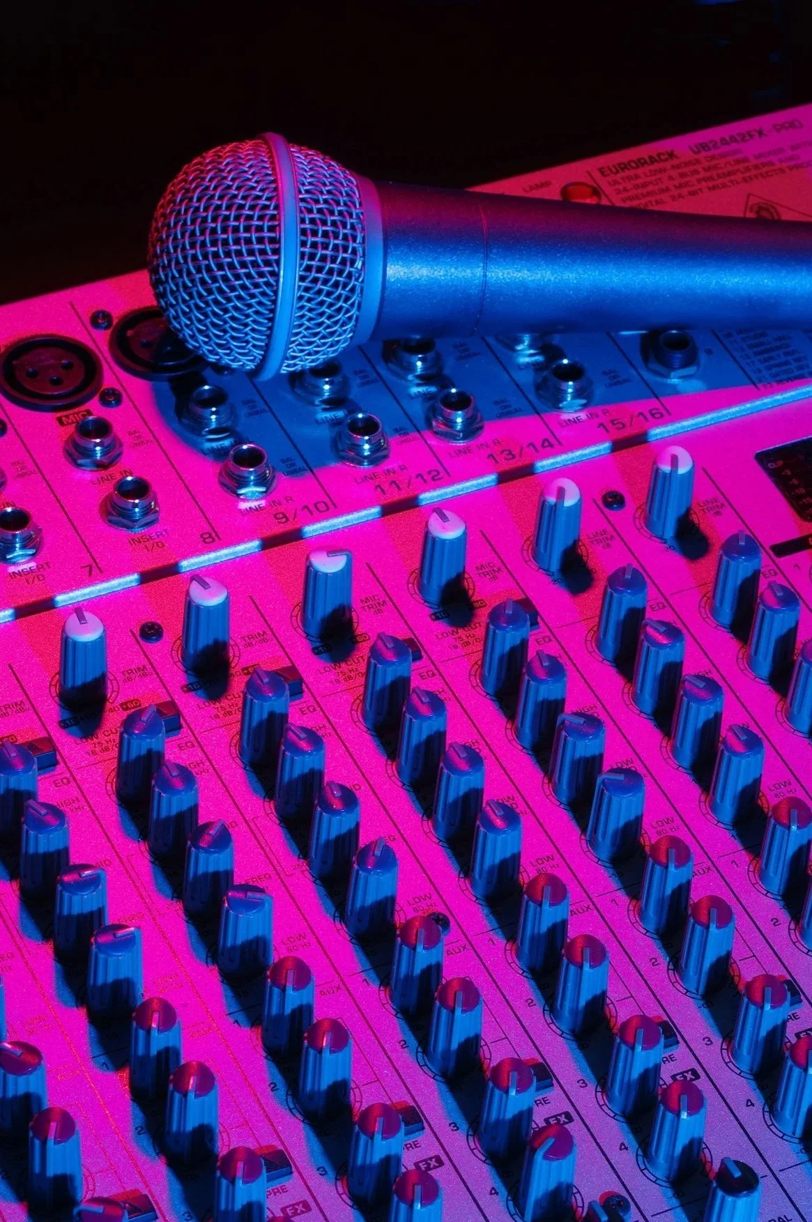 Close-up of a microphone resting on a professional audio mixer with colorful lighting.