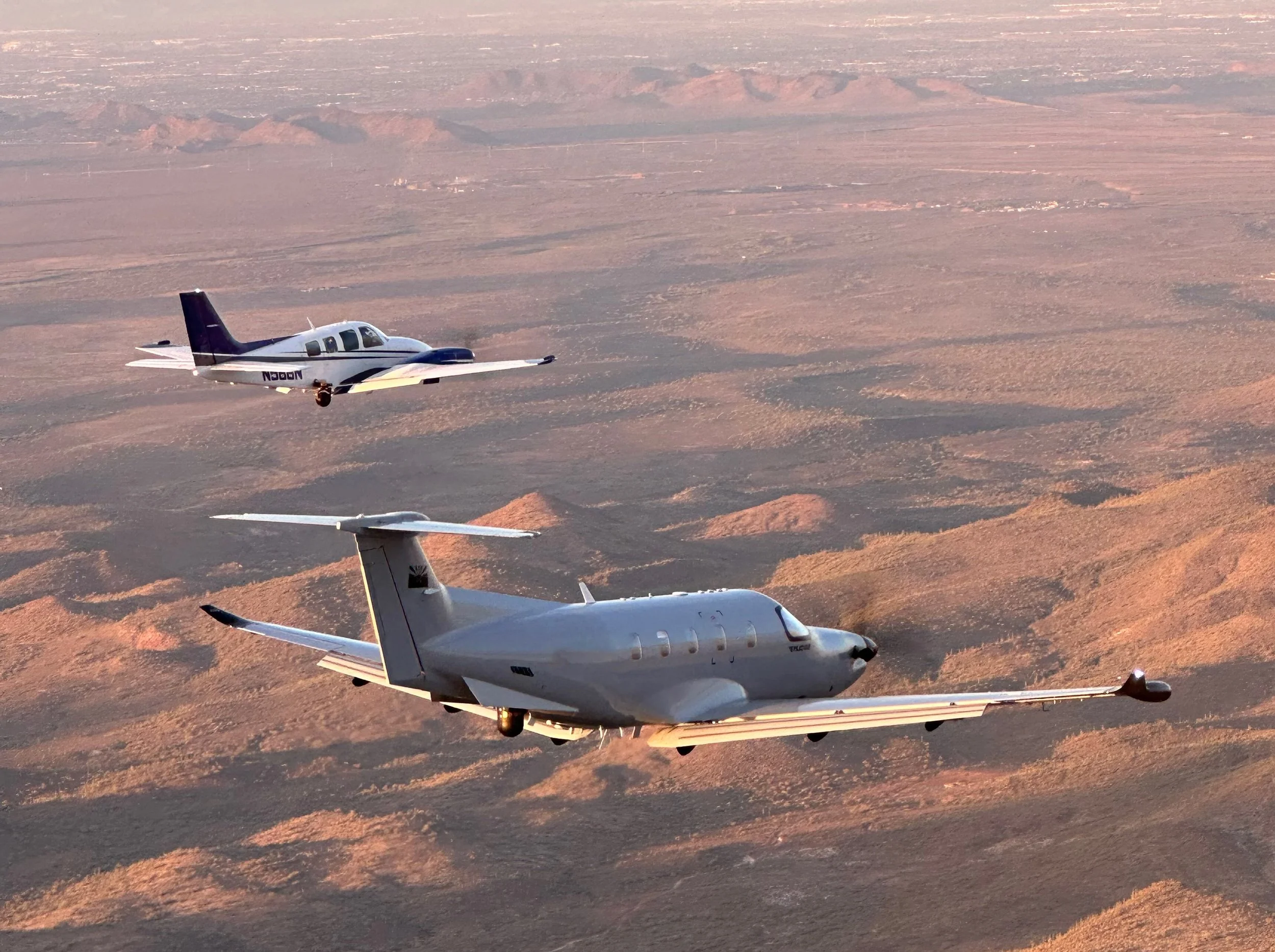Baron 58 photoship and Pilatus PC-12 over a desert landscape with mountains in the background during sunset.