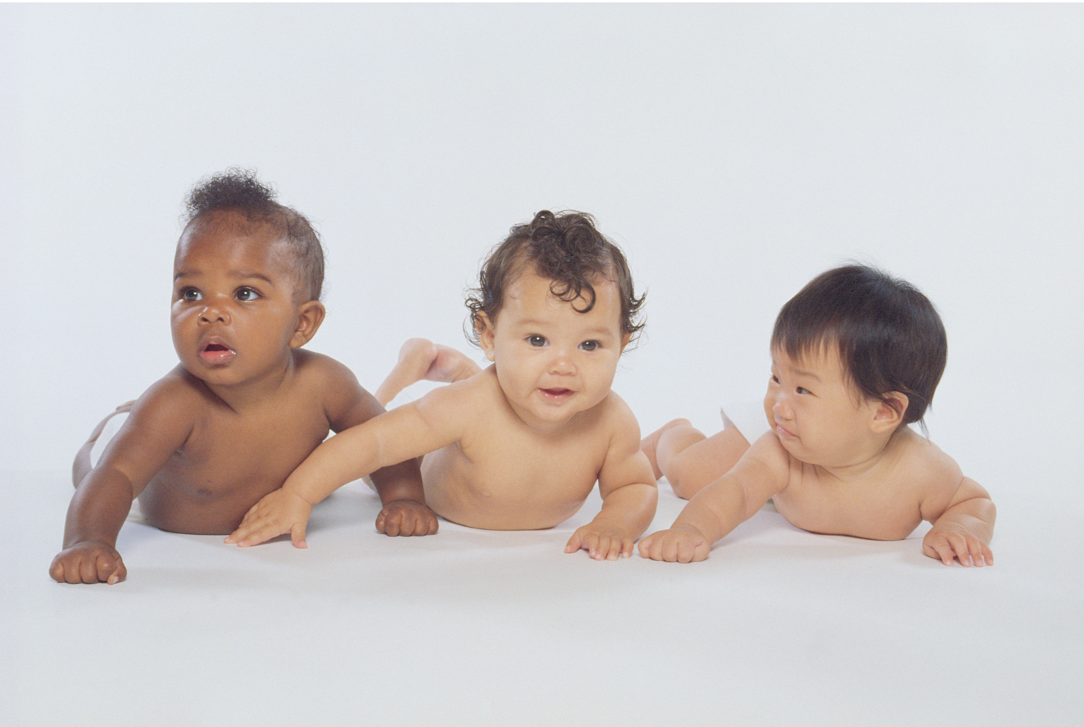 Three babies lying on their stomachs on a white surface against a plain white background.