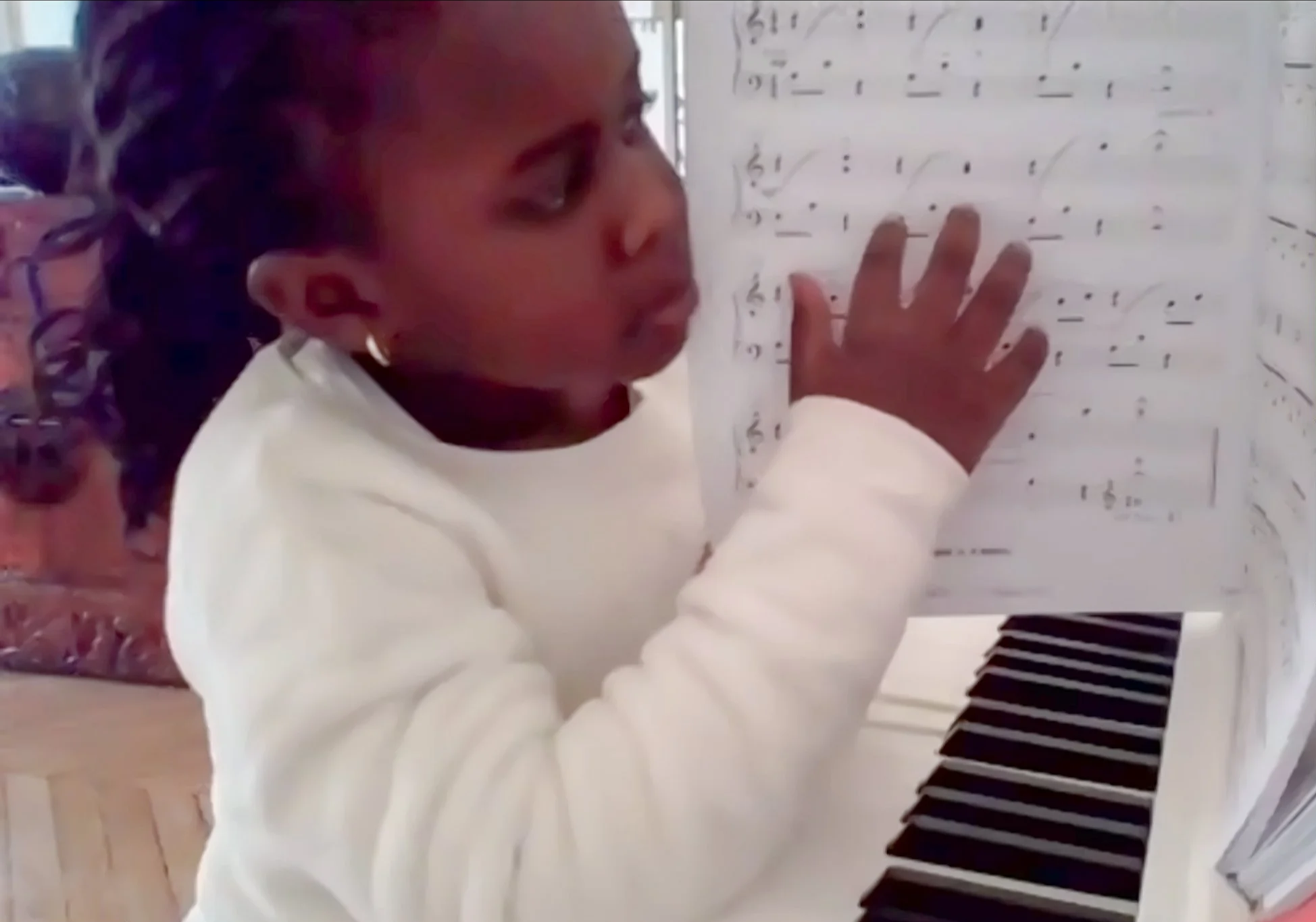 Child holding sheet music up to camera during piano lesson