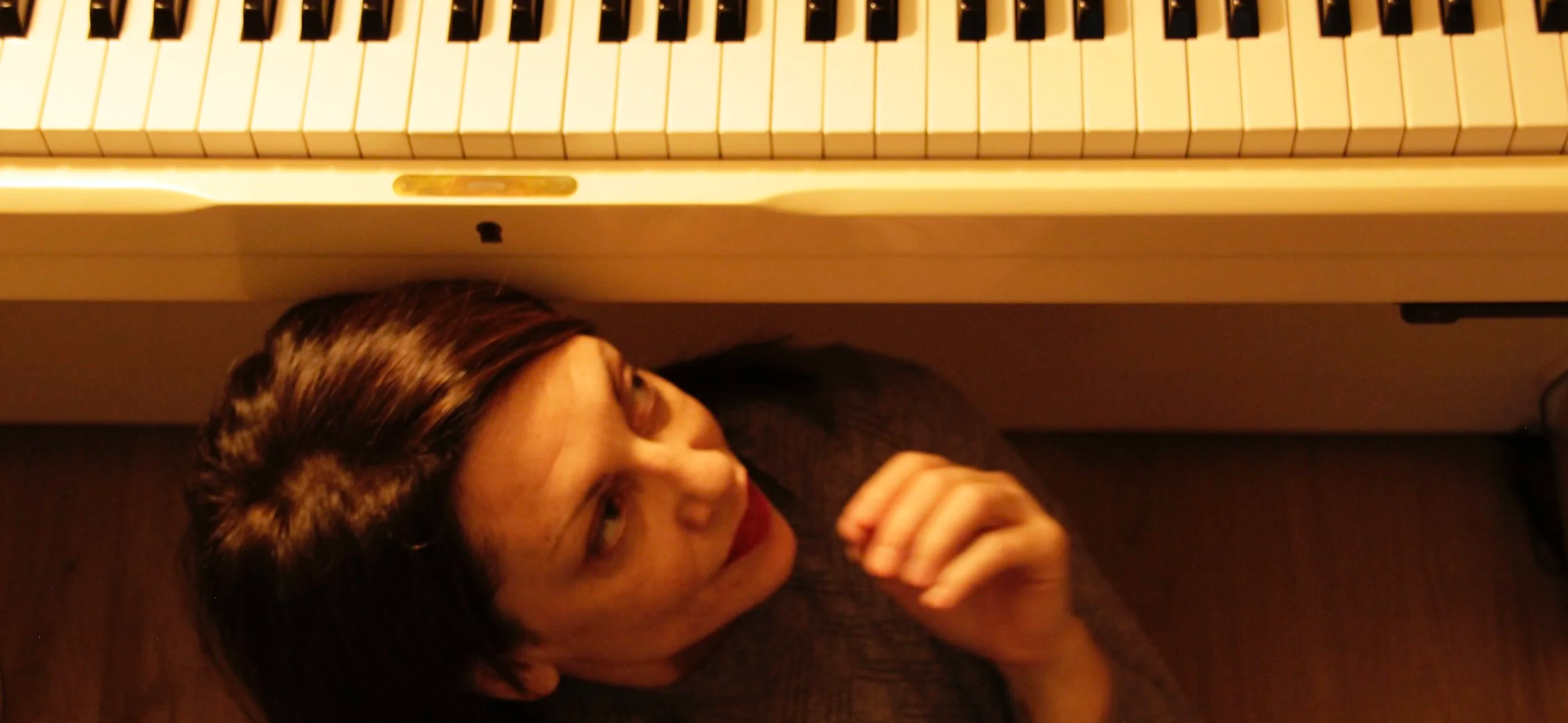 Teacher sitting under piano, looking up at keyboard
