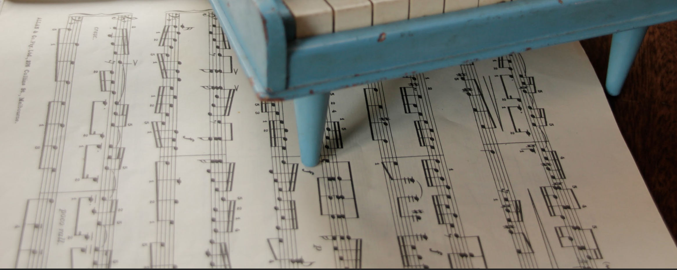 Corner of a blue toy piano on sheet music, header photo for Fees page