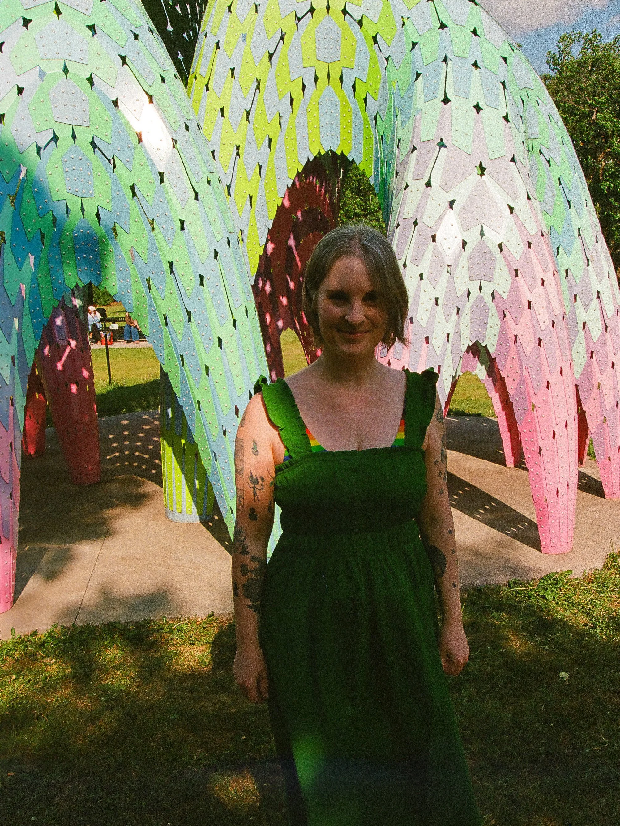 Photo of Jen from 2025  taken by Jeff Woodwardwearing a green dress standing next to the Vaulted Willow sculpture at Borden park.
