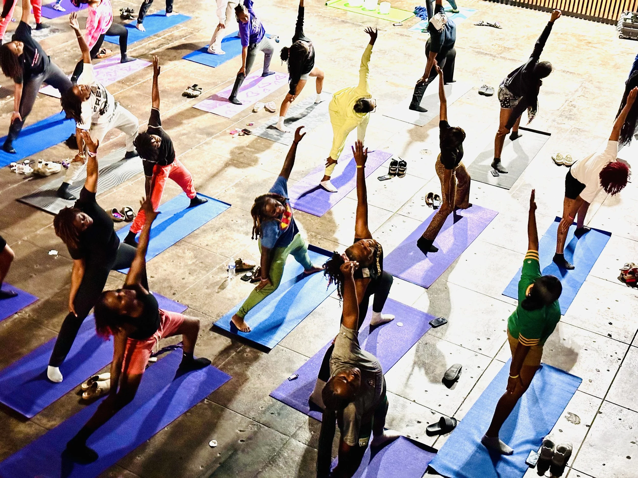 A group of people participating in a yoga class, practicing yoga poses on exercise mats outdoors during evening or night.