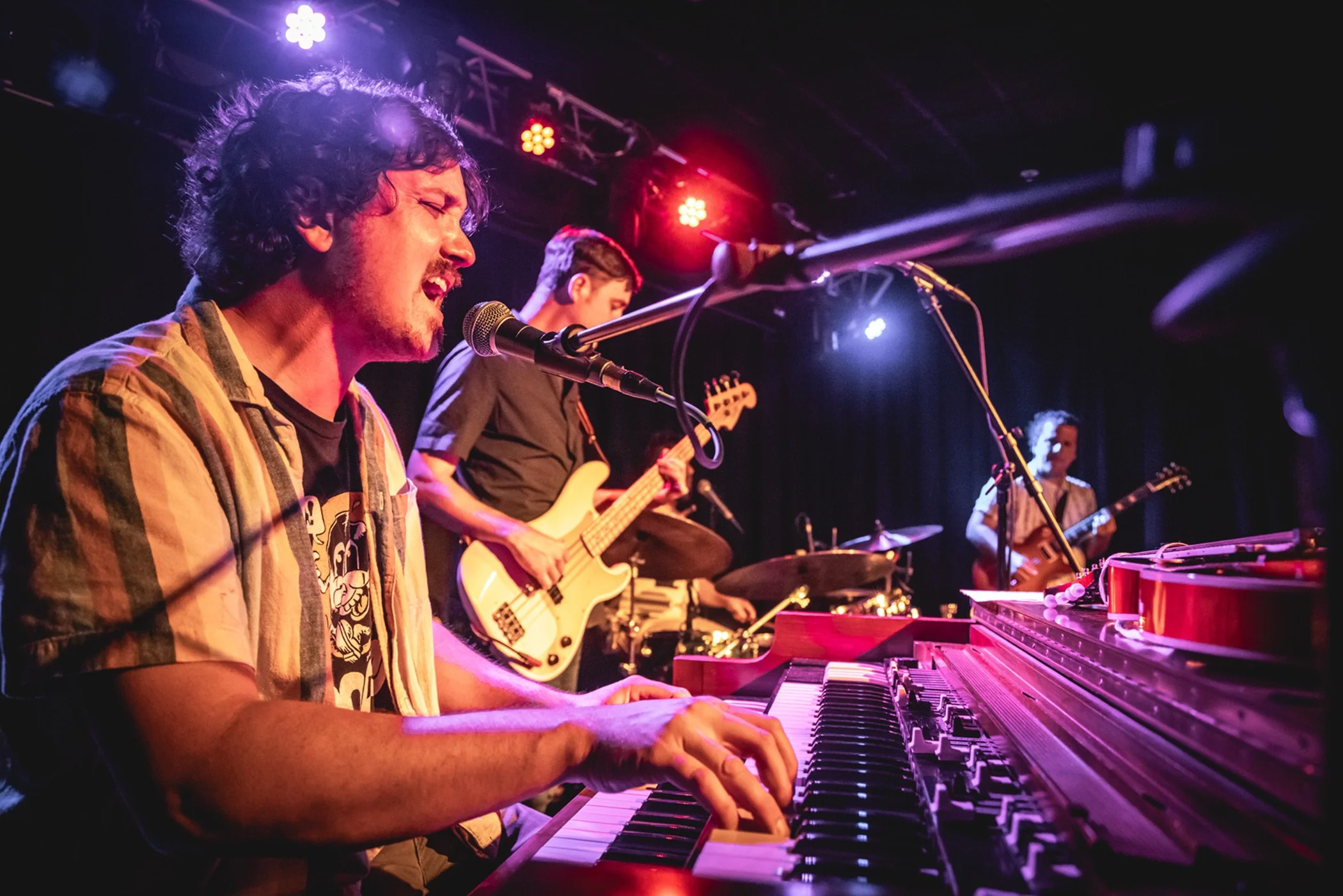 A live music performance of featuring the soul-rock band Cordelia Blue, with a keyboardist, guitarist, bassist, and drummer on stage under colorful stage lighting.