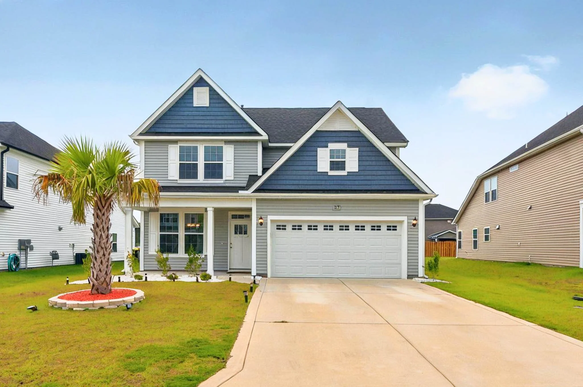 Two-story house with blue and gray exterior, white trim, attached garage, landscaped front yard with palm tree, green grass, and small bushes.