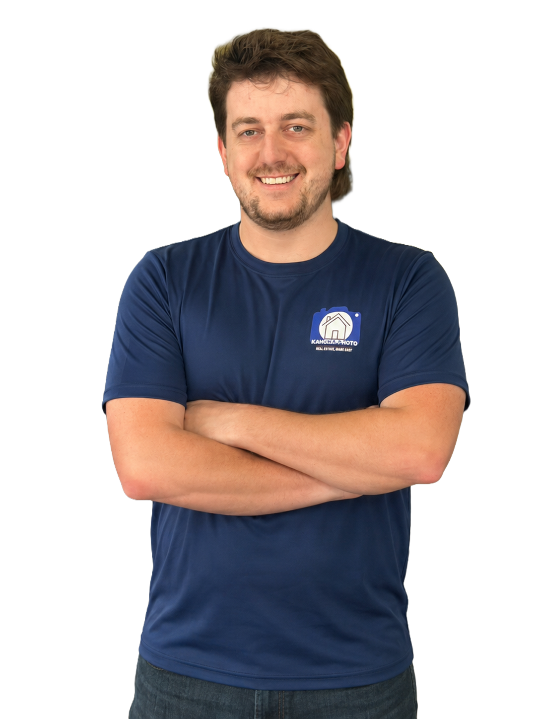 A young man with curly hair and a light beard, smiling, wearing a navy blue T-shirt with a logo on the chest that says "KAHUNA PHOTO" and features a house icon, standing against a white background.