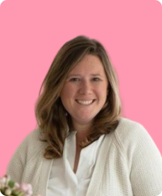 A woman with shoulder-length brown hair smiling, wearing a white sweater, against a pink background.