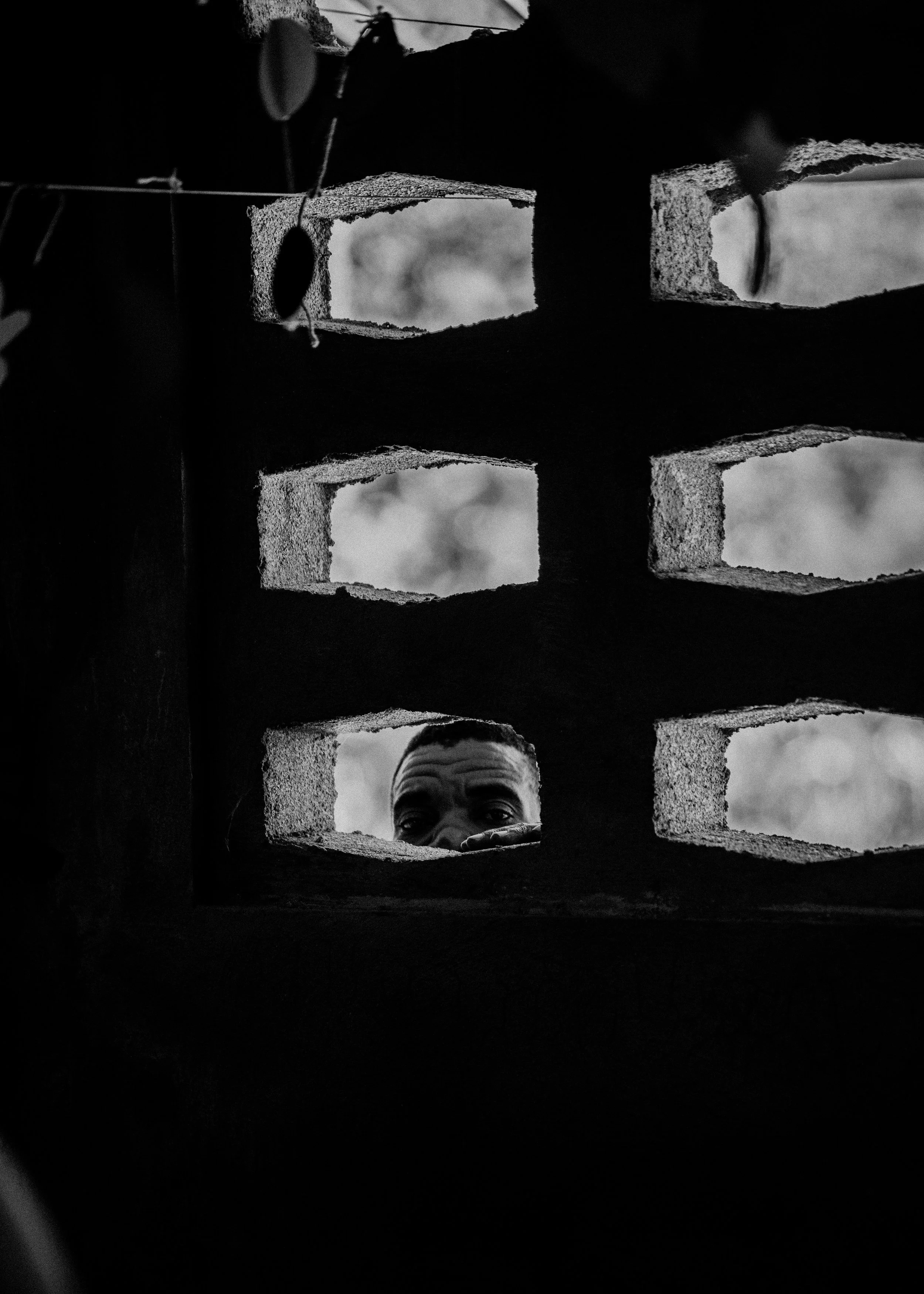 A person peering through a rectangular hole in a brick wall with a grid pattern, with only their eyes and part of their forehead visible.