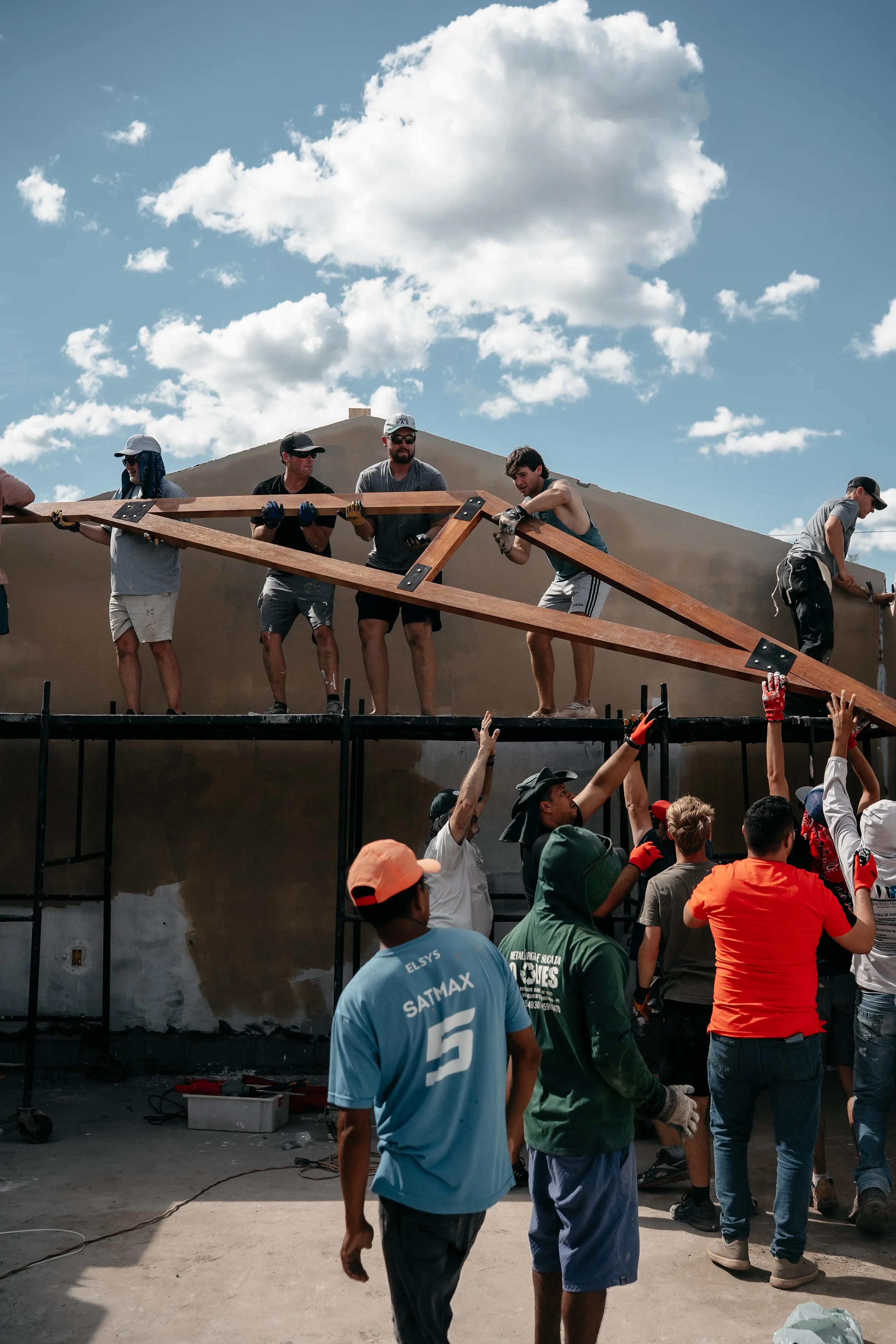 Group of people working together to build a wooden structure outdoors, with a cloudy sky overhead.