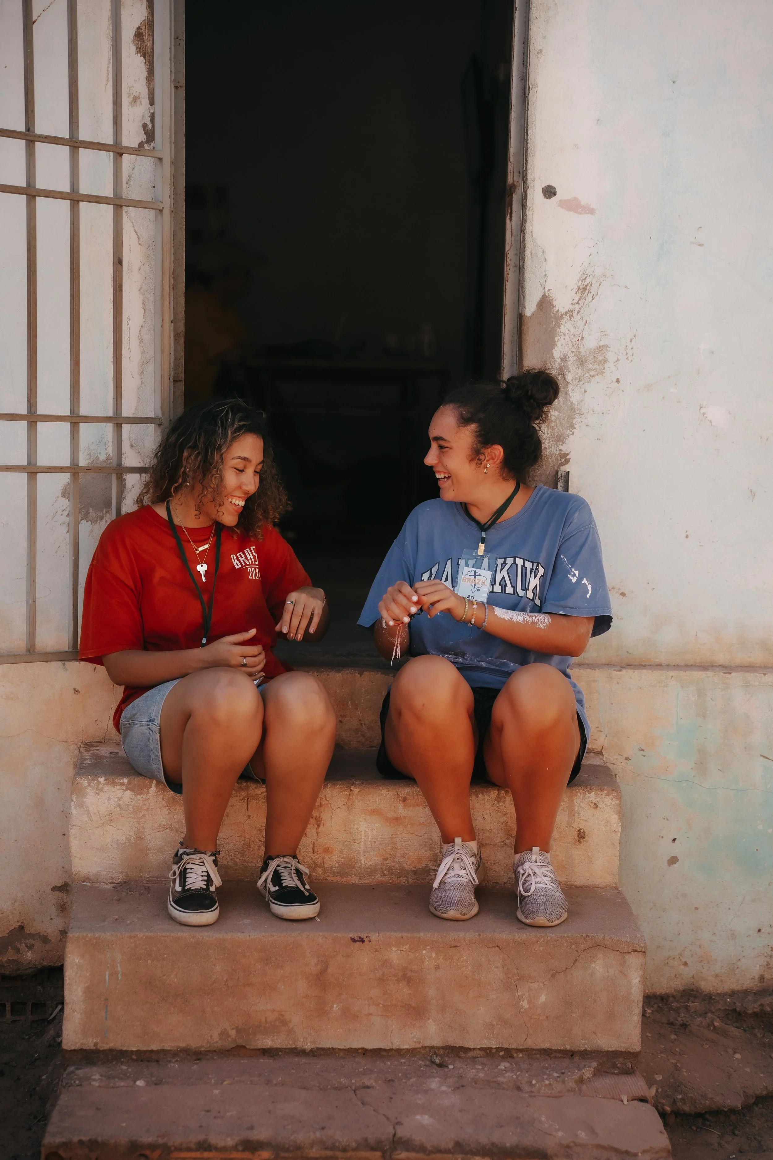 Two young women sitting on steps outside a building, smiling and laughing together.