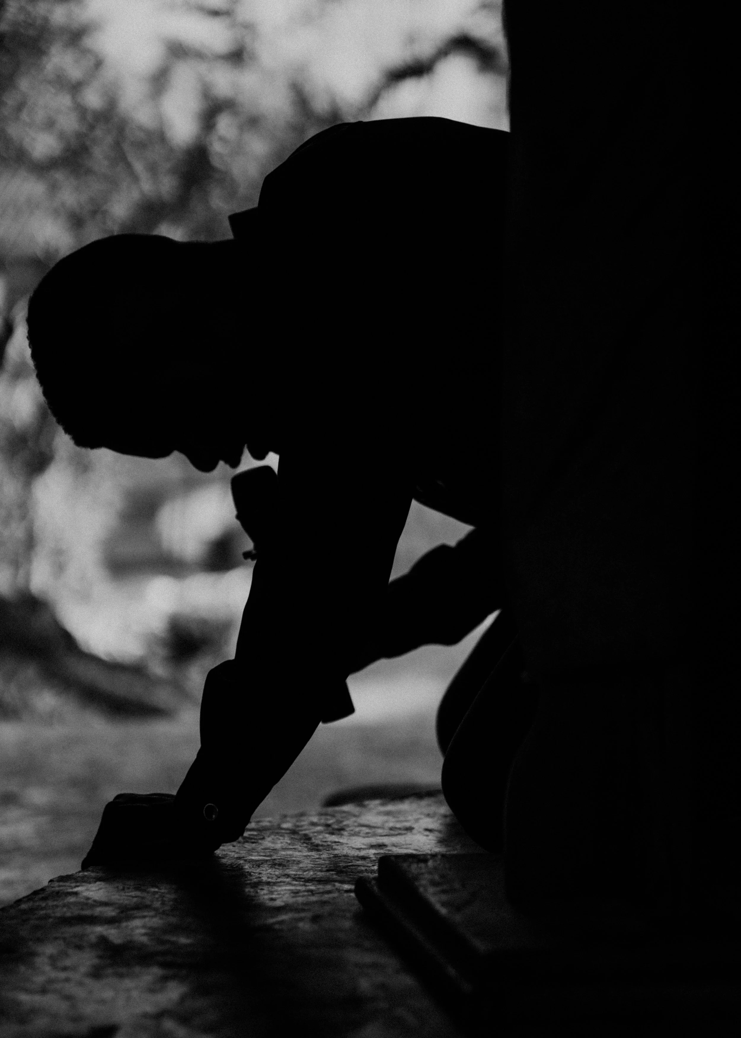 Silhouette of a person playing a guitar outdoors in black and white.