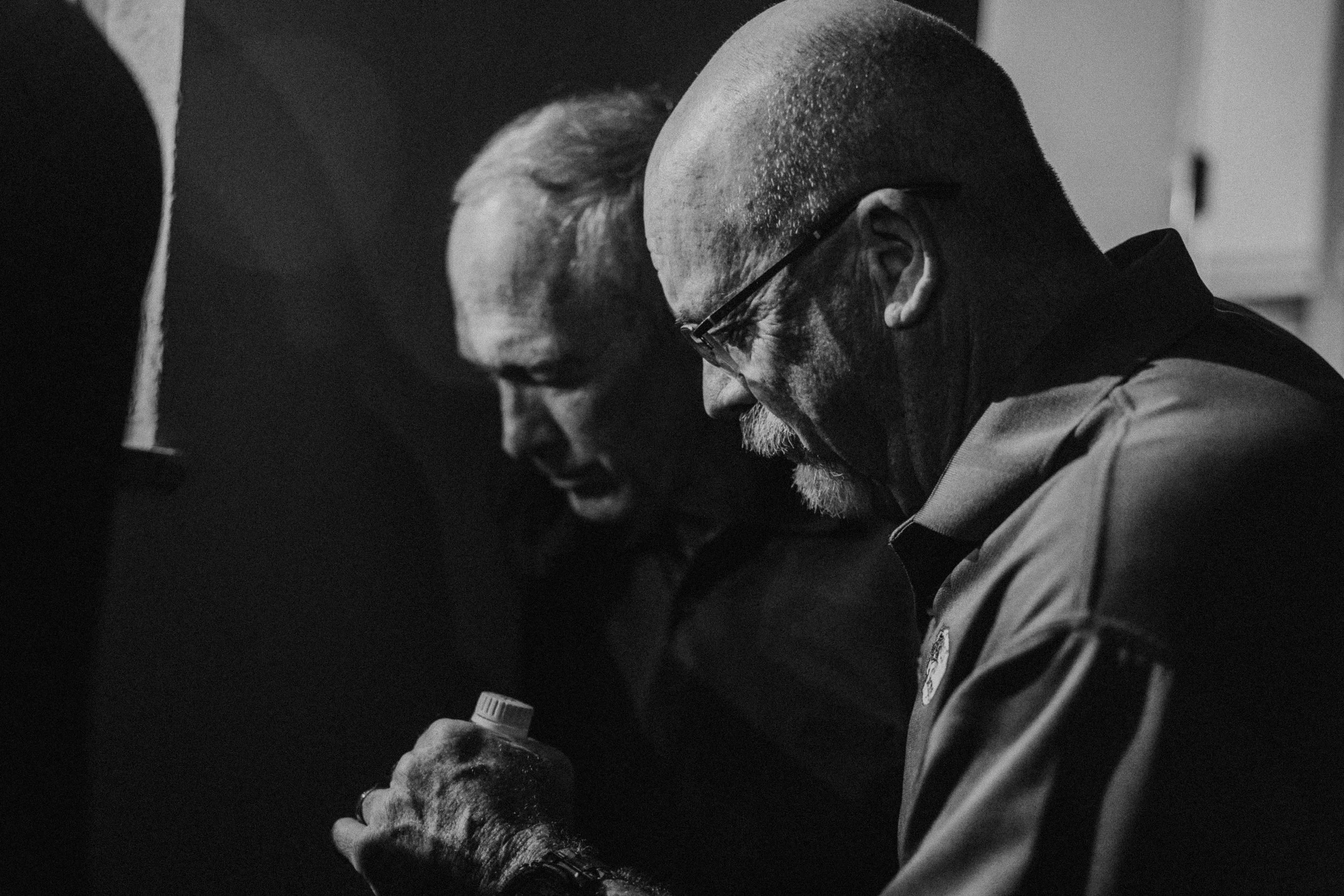 Two men are looking at a small object held in one man's hand in a close-up, black-and-white photo.