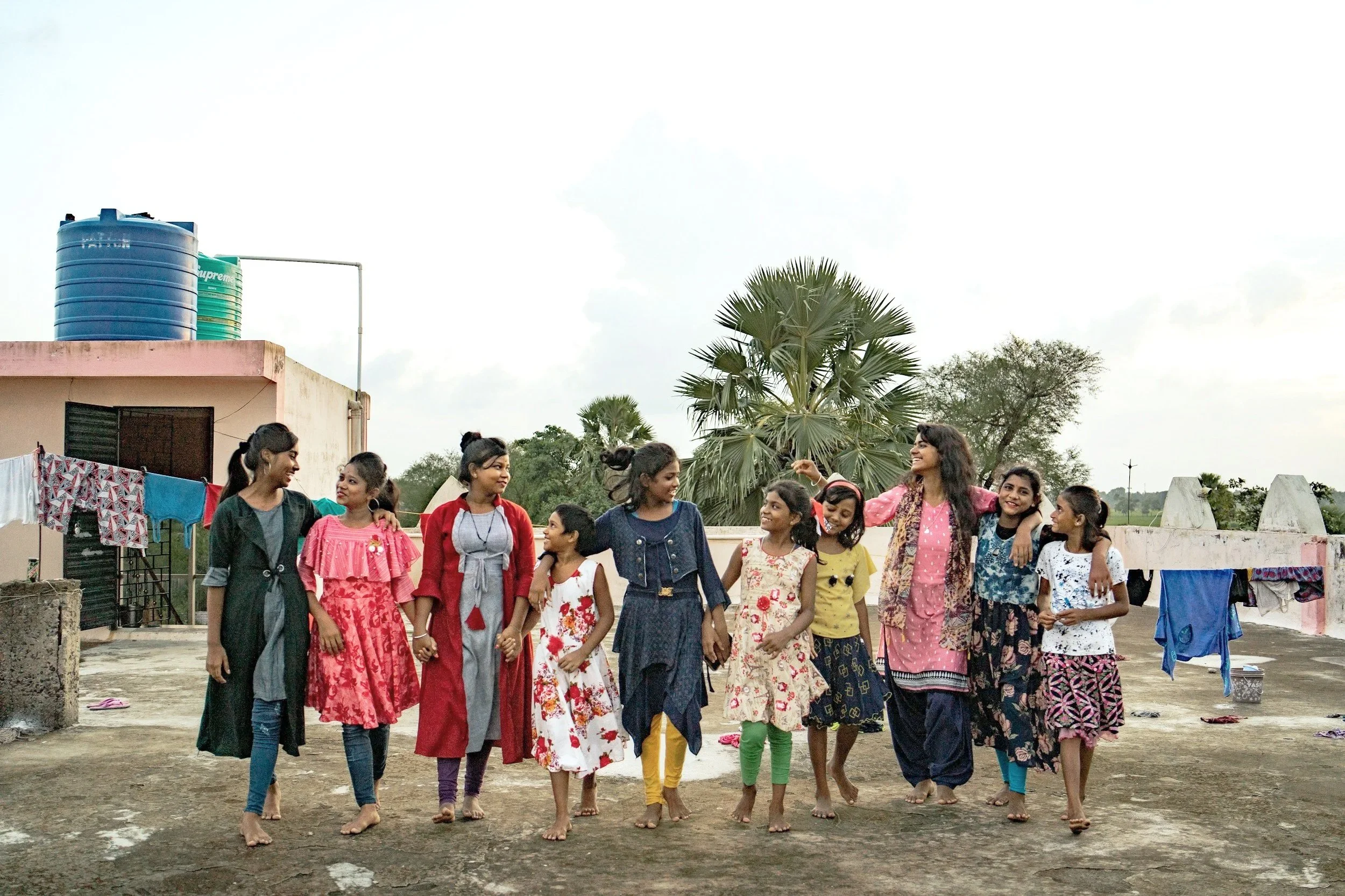 A group of women and children walking on a rooftop, smiling, and engaging with each other.