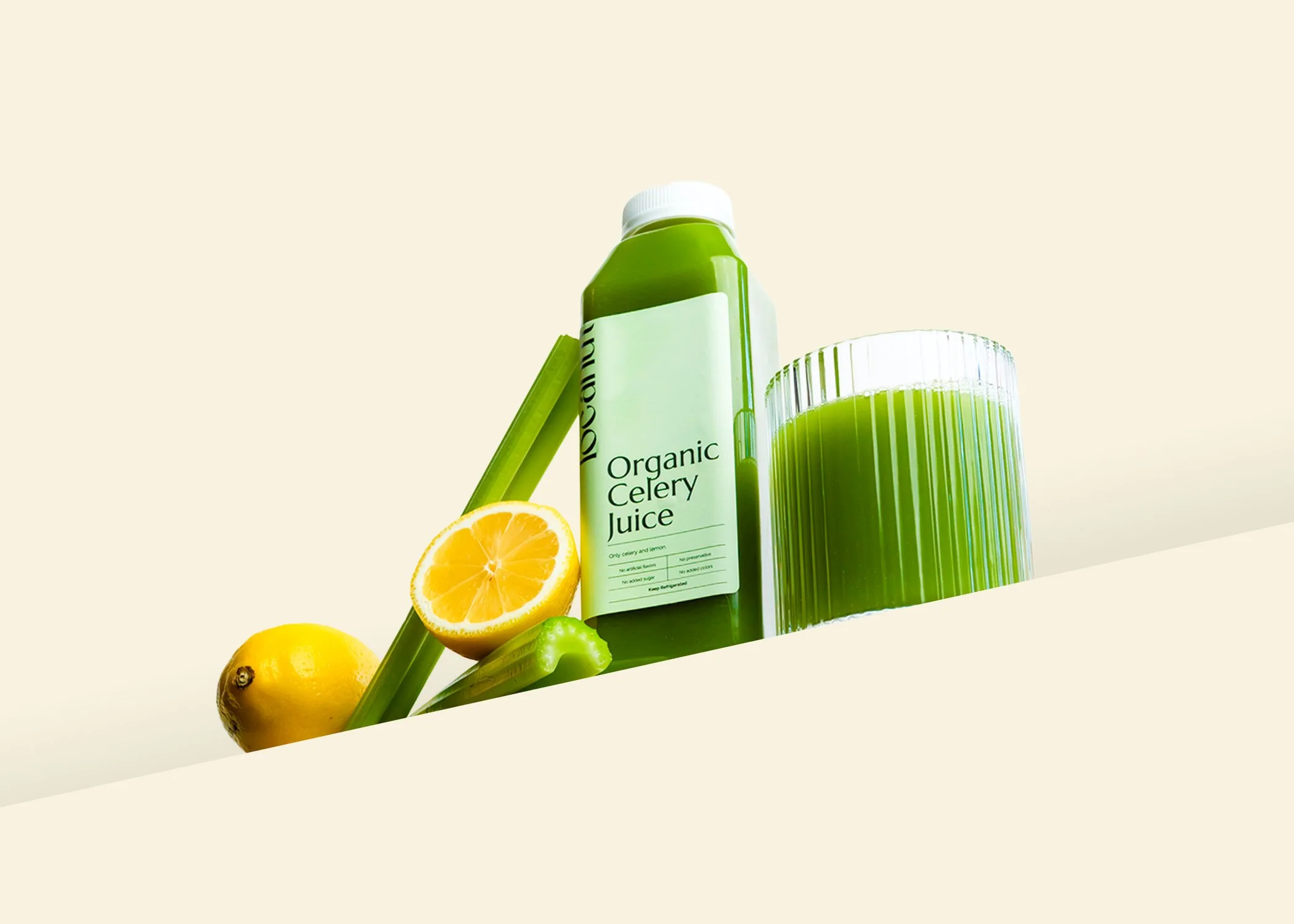 Bottle of organic celery juice with a glass, lemons, and celery stalks on a light background.