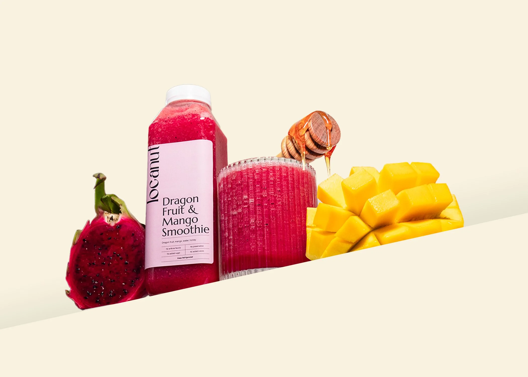 Bottle of dragon fruit and mango smoothie next to cut dragon fruit, sliced mango, and a glass with honey dipper.