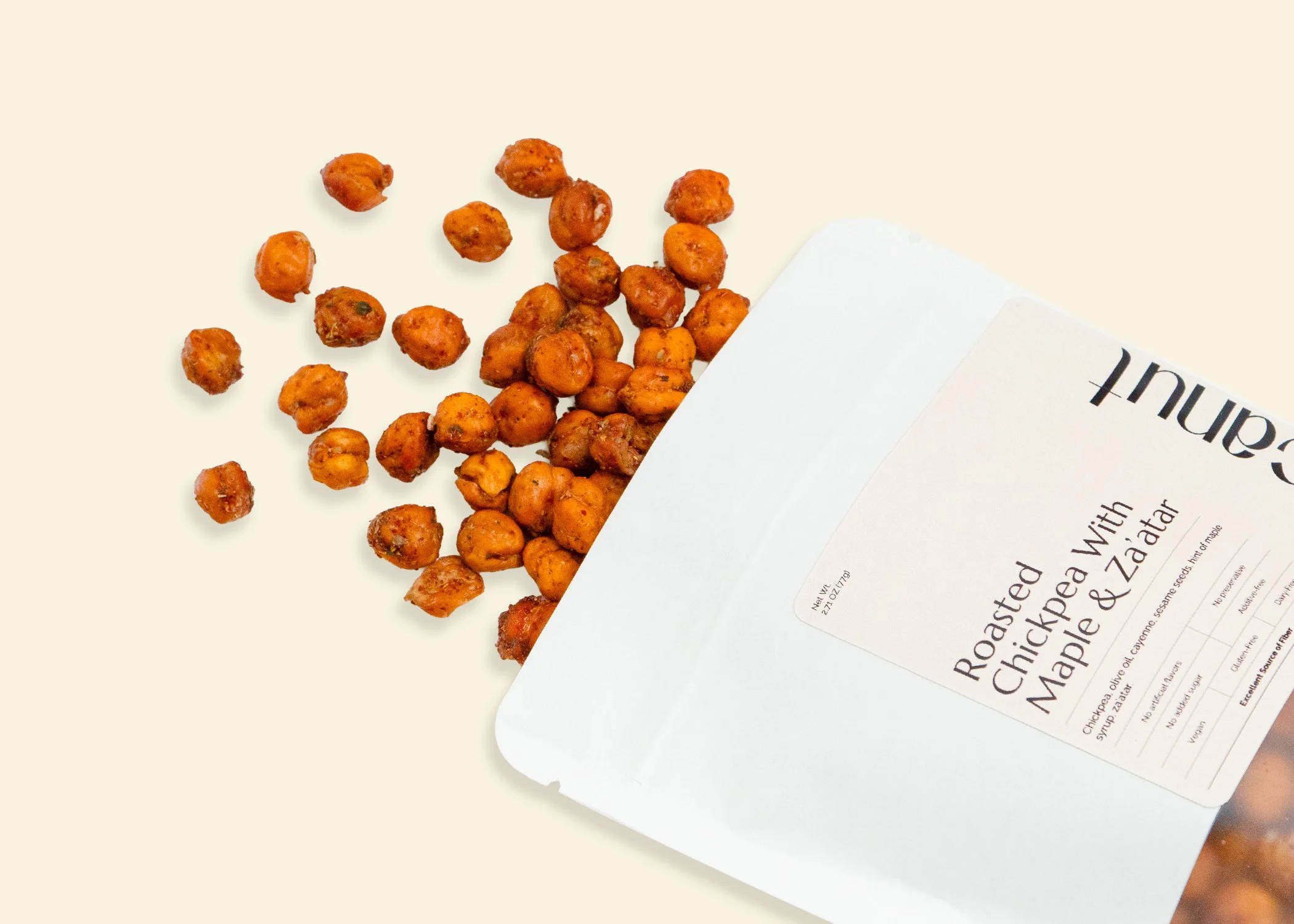 A bag of roasted chickpeas flavored with maple and za'atar spilling out of its packaging on a light background.