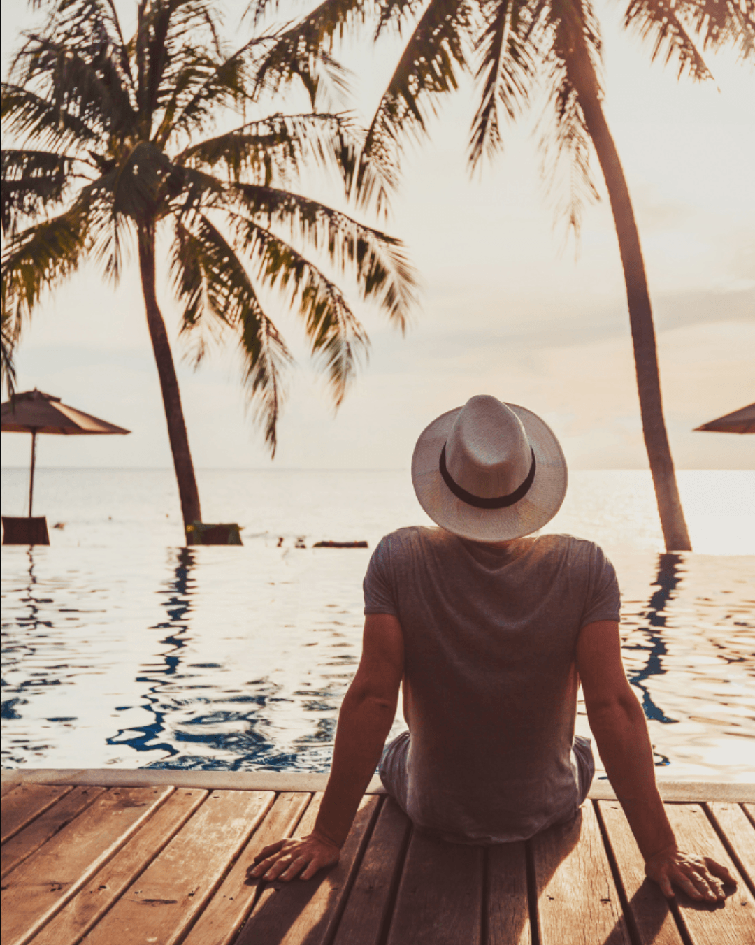 Person relaxing by an infinity pool with ocean view and palm trees at a tropical resort