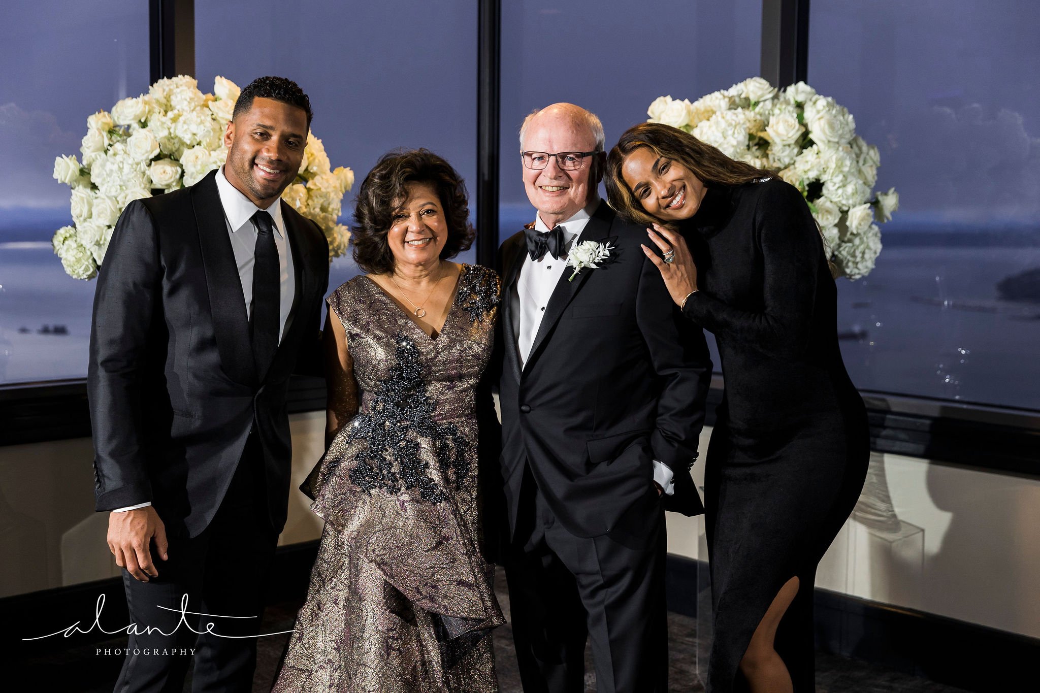 Group of five people dressed in formal attire, standing indoors with large floral arrangements in the background.