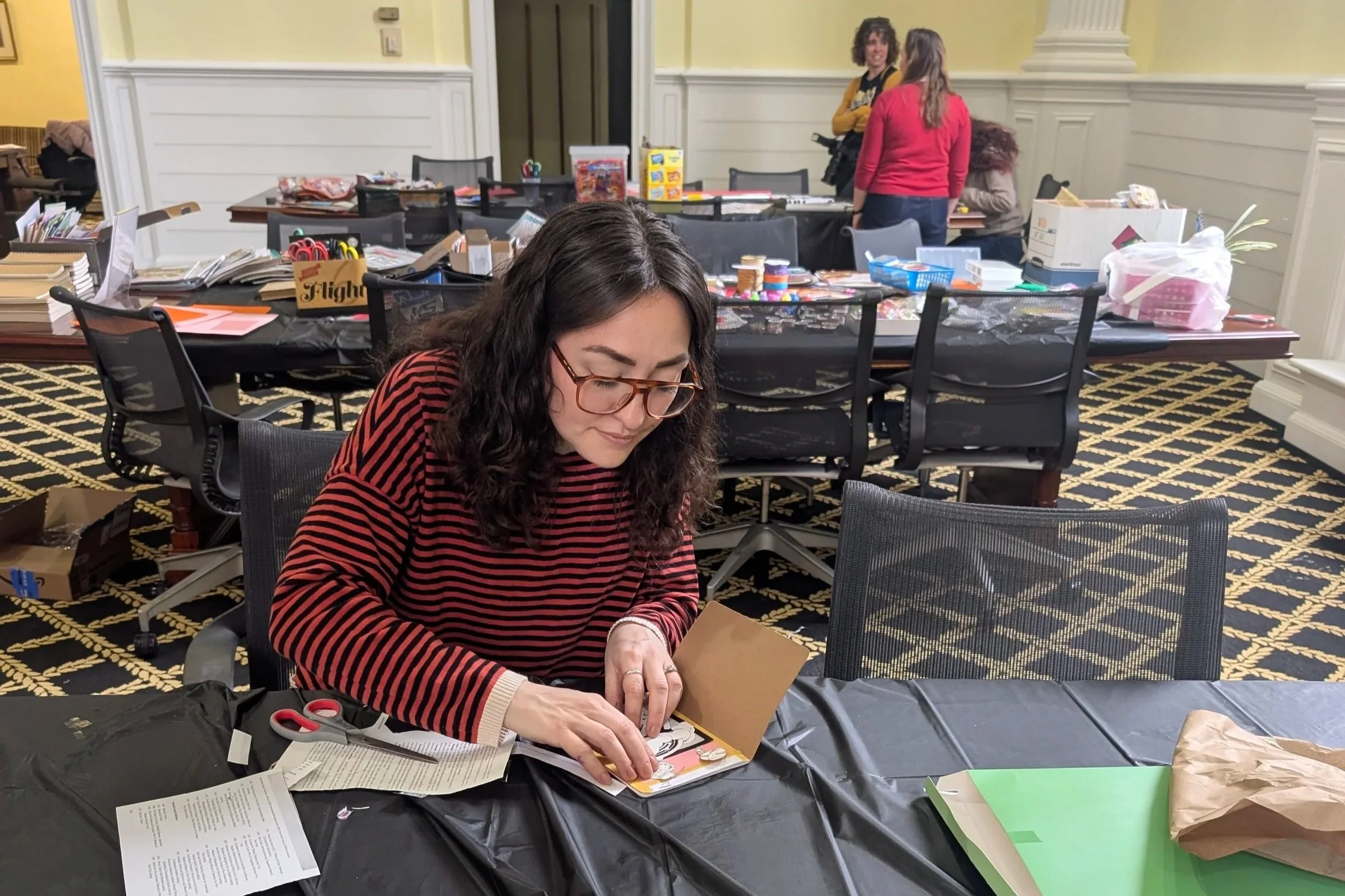 A student working at a table with three other students talking and working at another table.