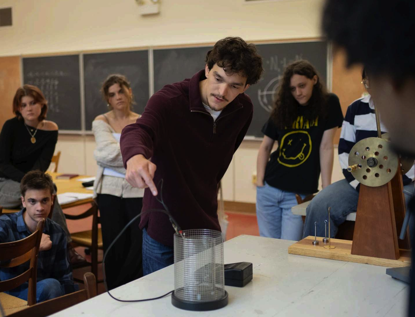 six students watching another student conducting an experiment in a classroom