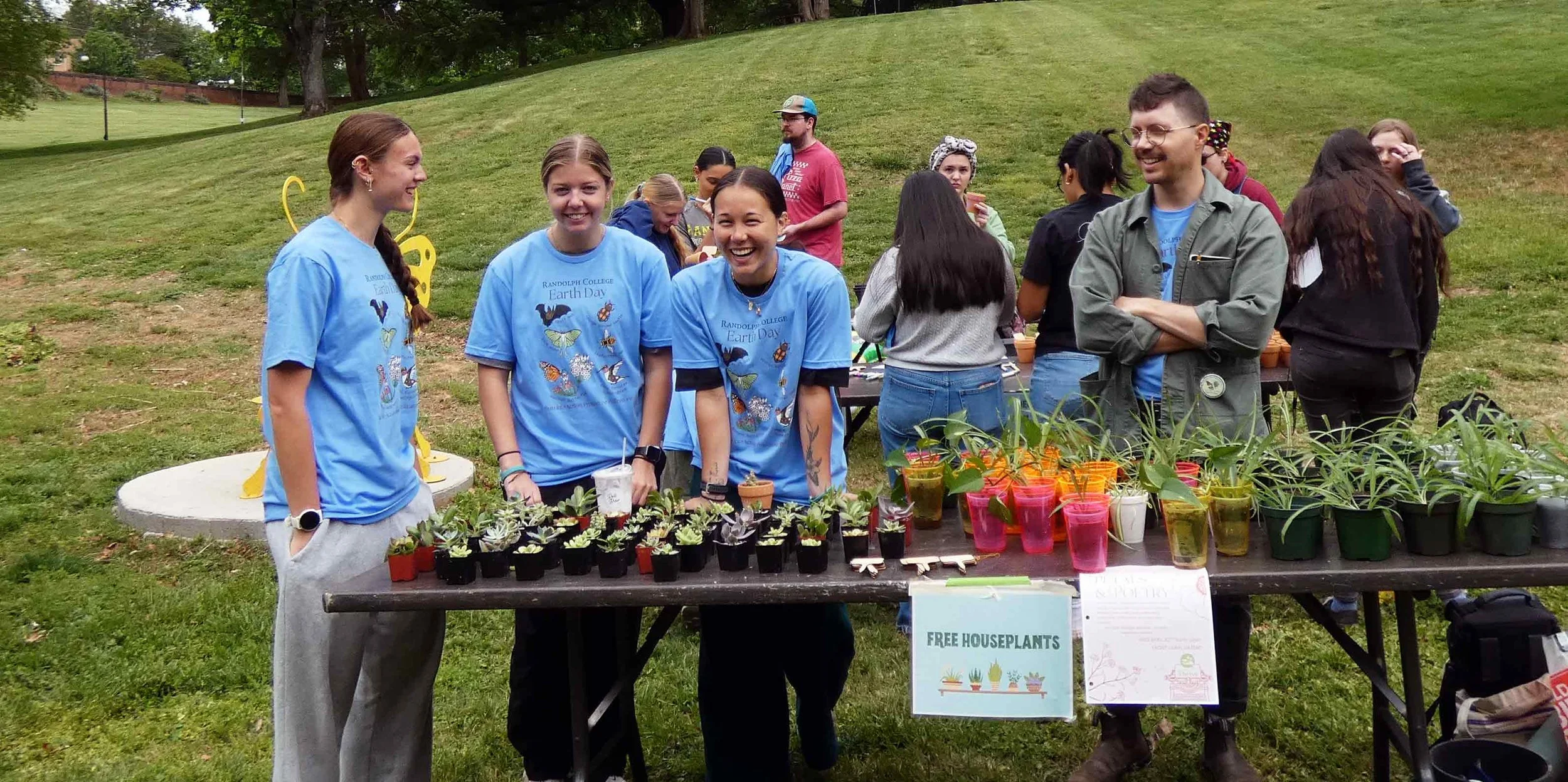 students and staff at a table with plants. the tables has a sign that reads "Free Houseplants".