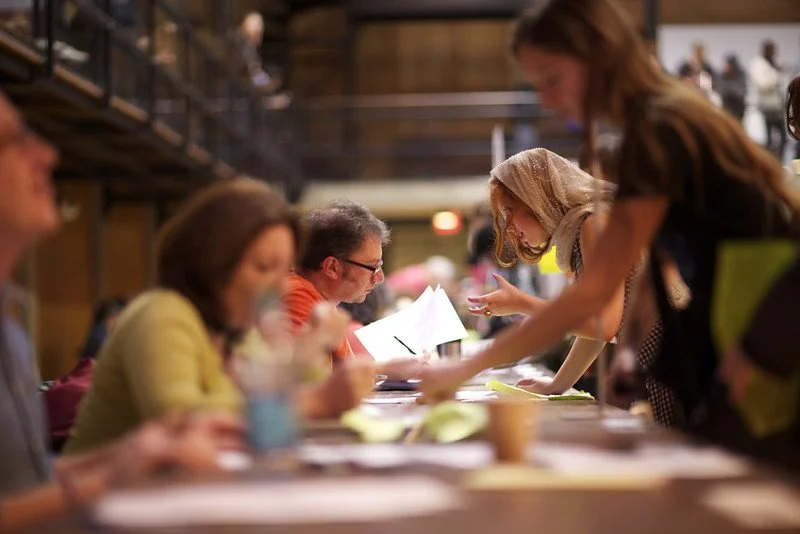 four people in discussion sitting at a table with papers and cups