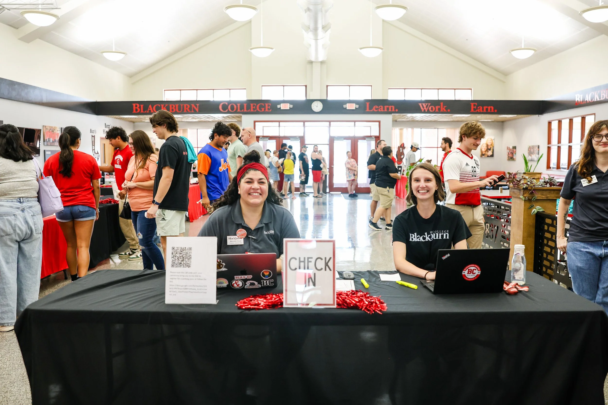 Two Blackburn College students at a table during Move In Day. Many students are in the background.