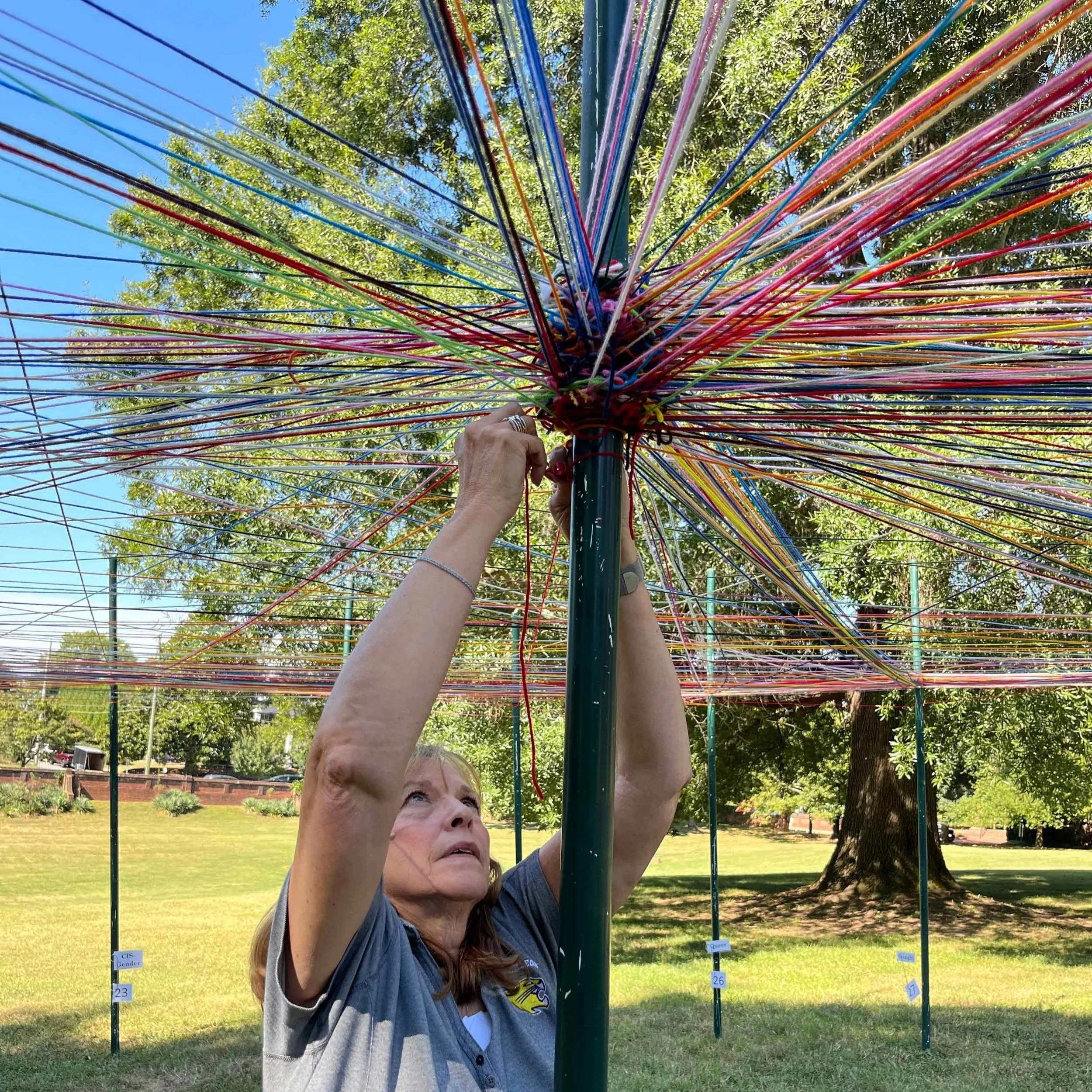 a woman tying multi-color yard to a pole