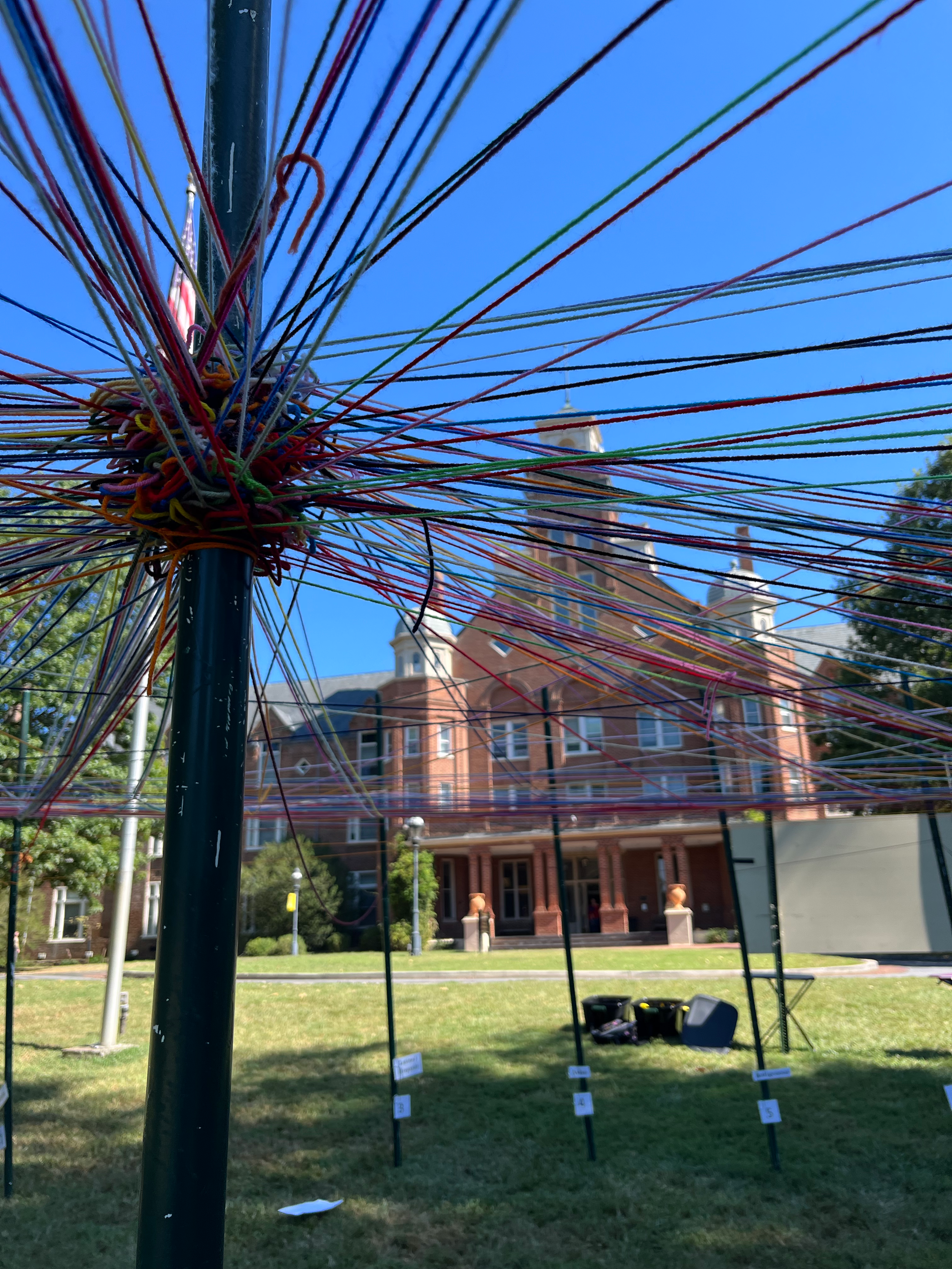 multi-color yard intertwined and wrapped around a pole with college building in background